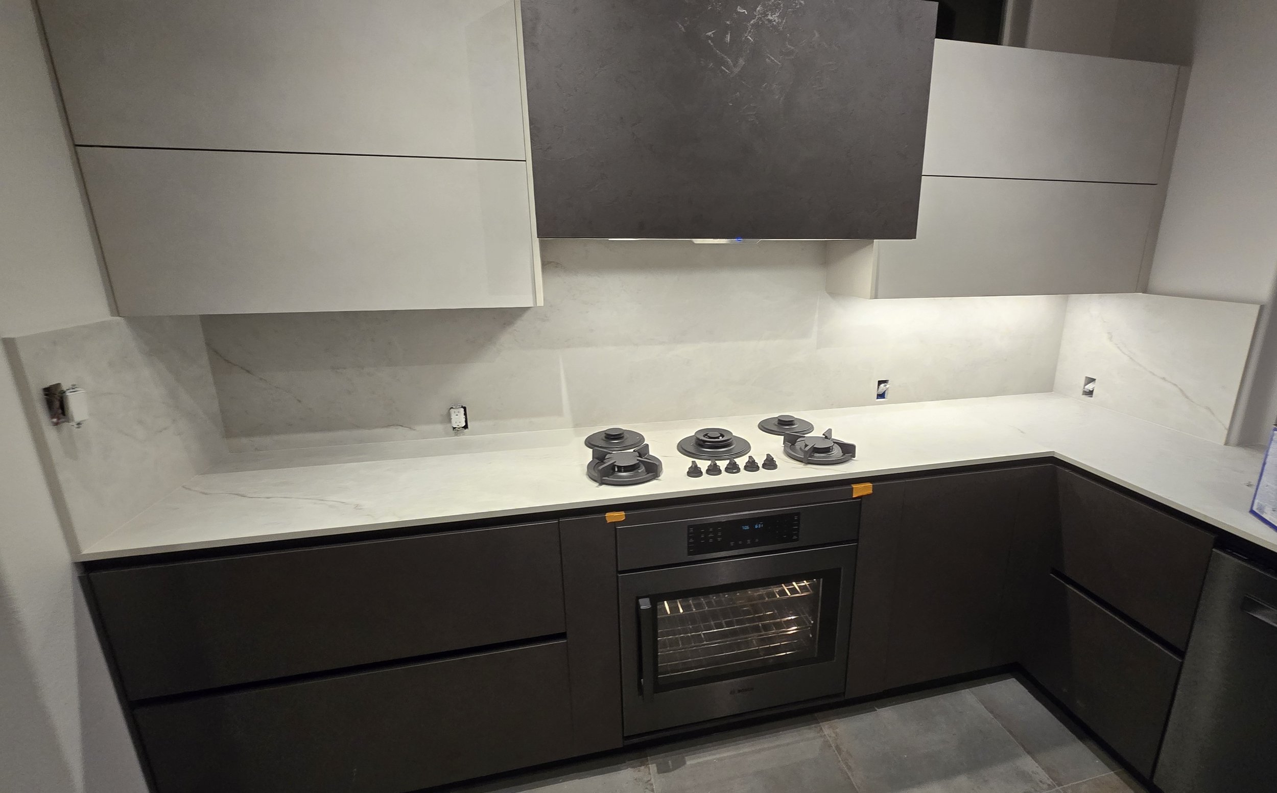 Modern kitchen with gray cabinetry, white marble countertops, and a built-in oven, stove with four burners, under-construction with open wall outlets.