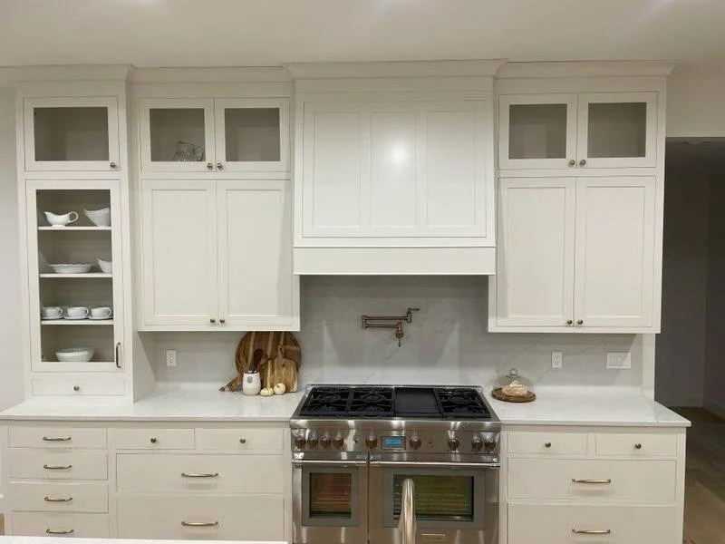White kitchen cabinets with a gas stove, open shelves with dishes, and a marble countertop.