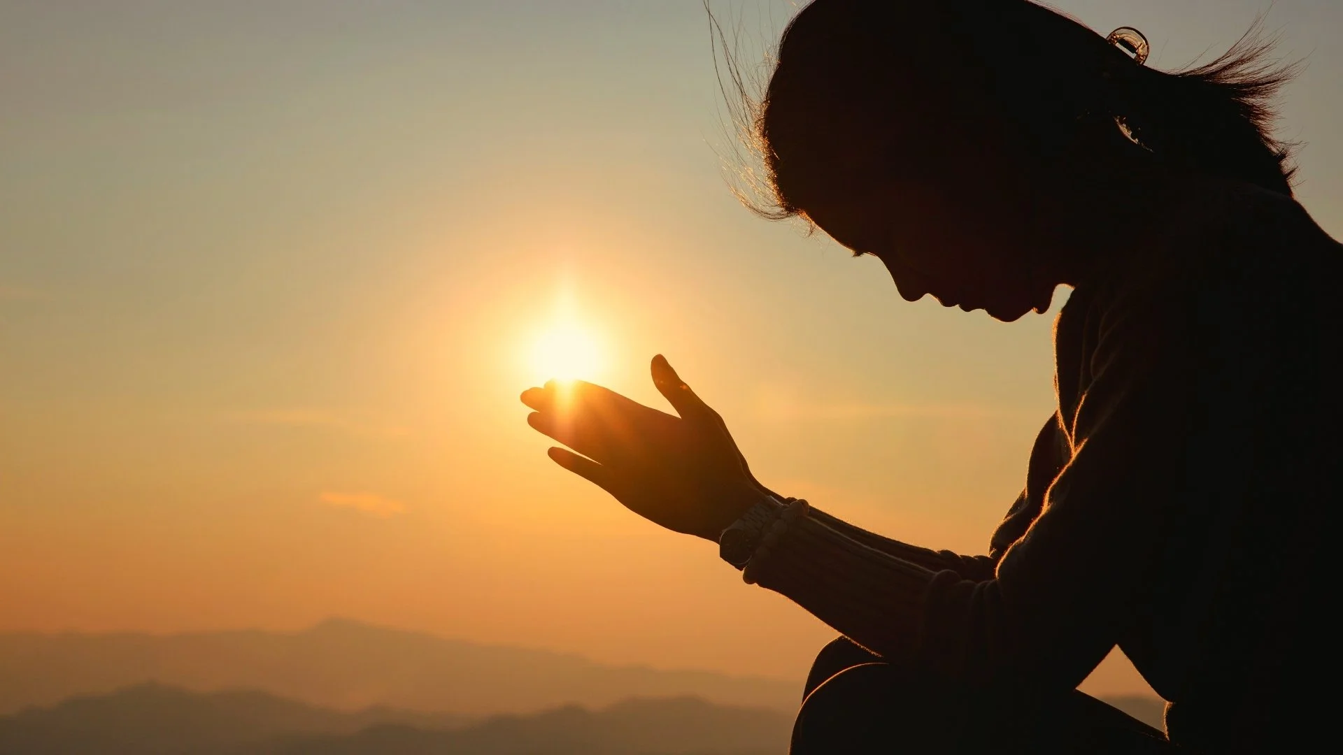 Silhouette of a woman in prayer against a sunset sky