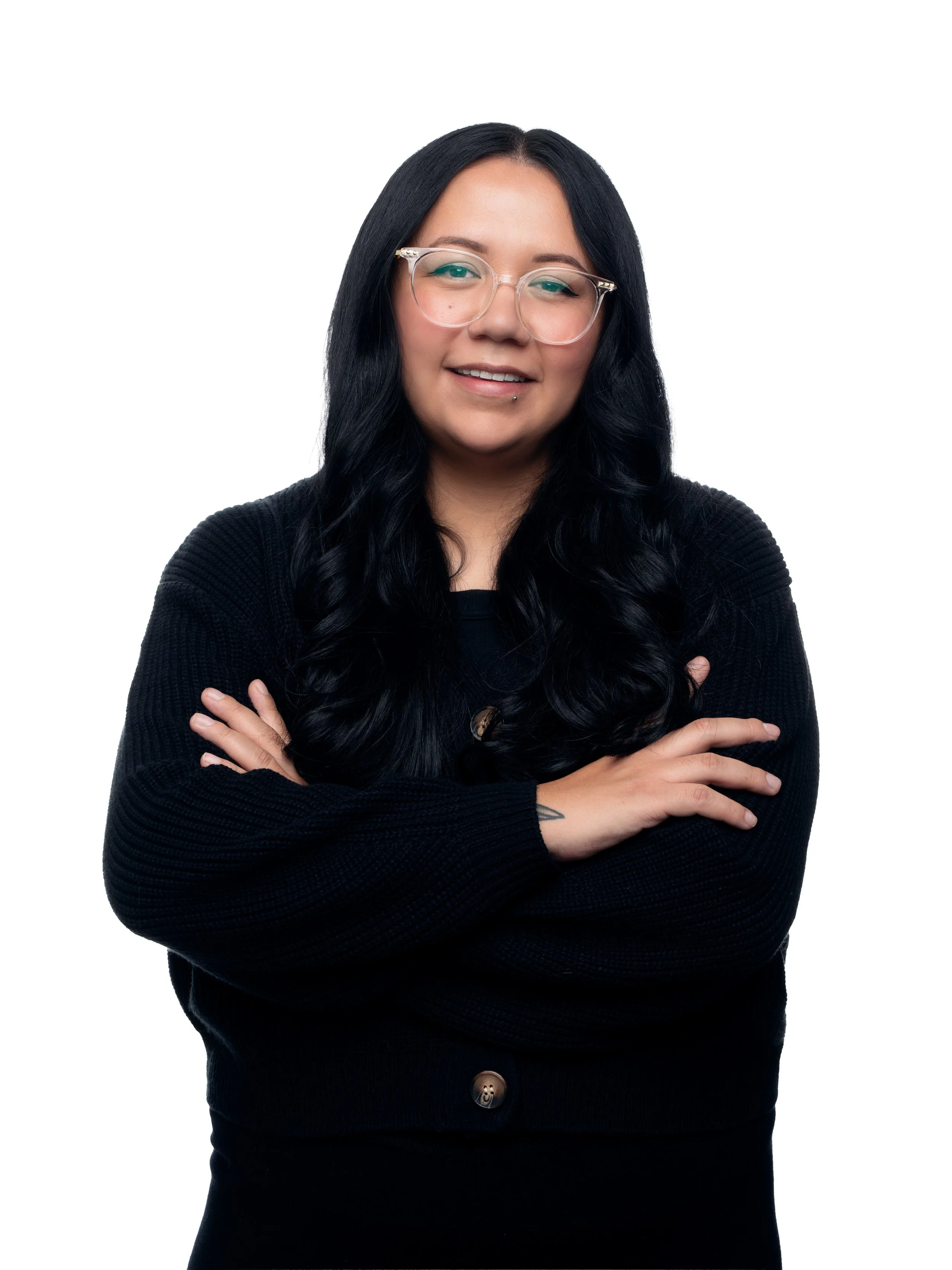 A woman with long black hair, wearing glasses and a black sweater, crossing her arms and smiling at the camera.