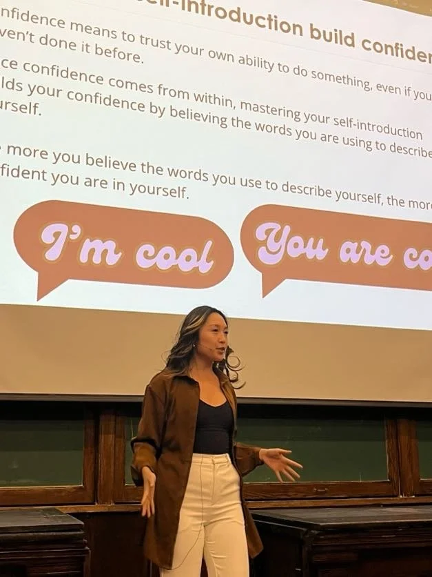 A woman giving a presentation in front of a projected slide that discusses building confidence through positive affirmations, with speech bubbles saying 'I'm cool' and 'You are cool'.