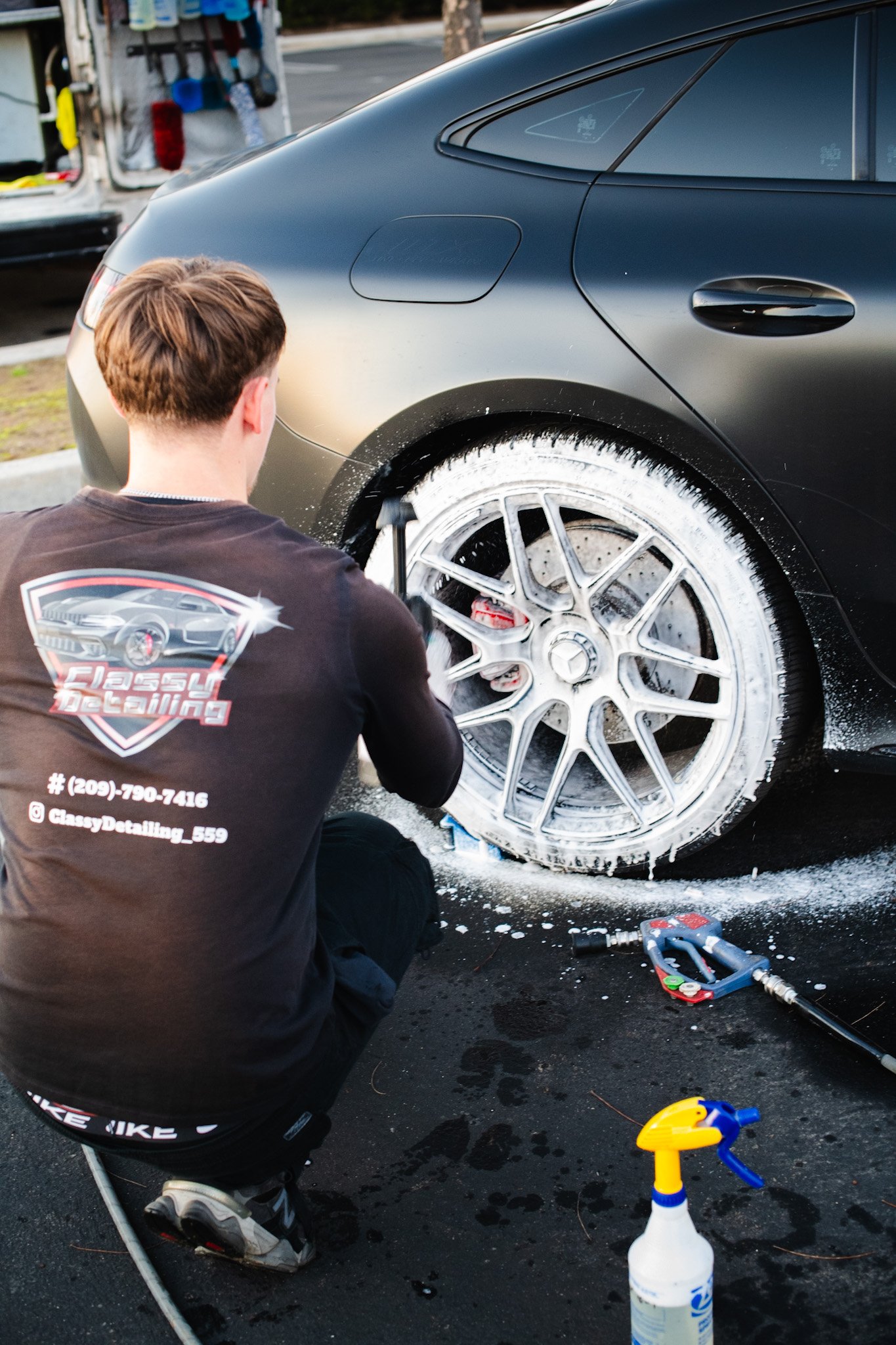 A person detailing a black Mercedes-Benz sports car wheel with brake cleaner using a foam cannon