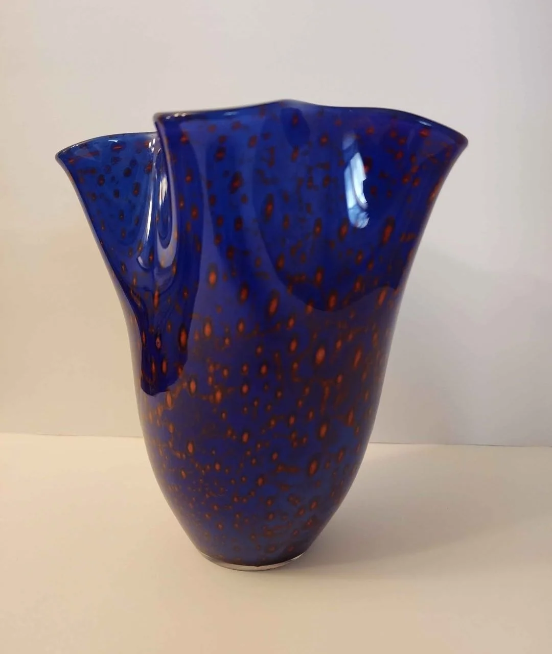 Blue glass vase with orange spots and a wavy, irregular rim.