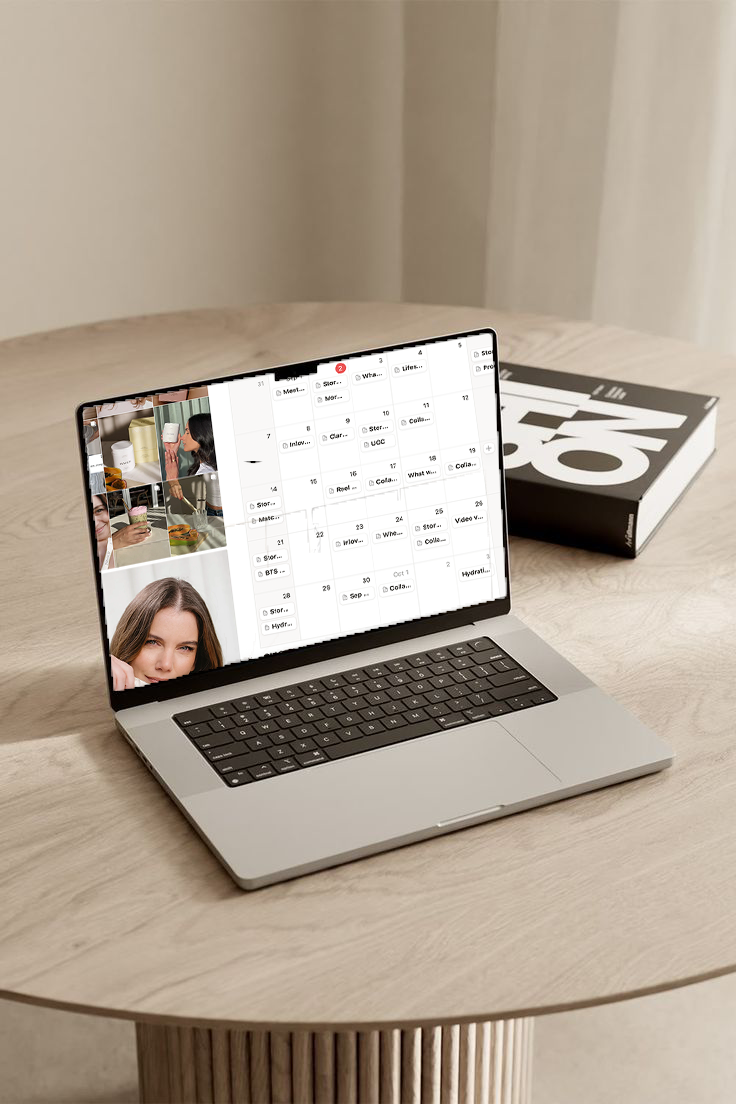 A laptop on a wooden table displaying a calendar and social media photos, with a large book titled 'ON' beside it.