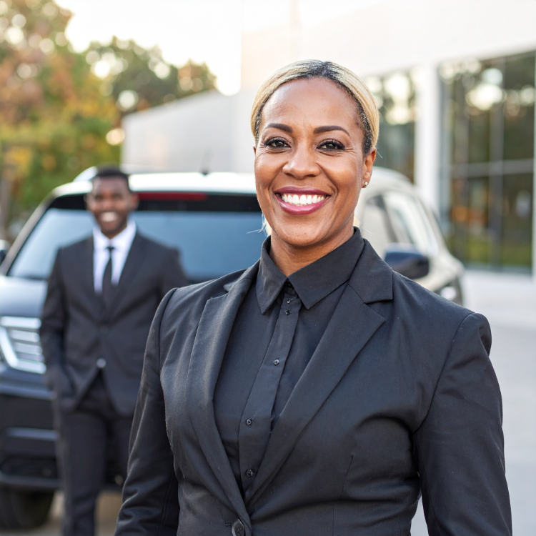 female african american suv driver smiling at the camera with a young african american man leaning agains a black SUV.
