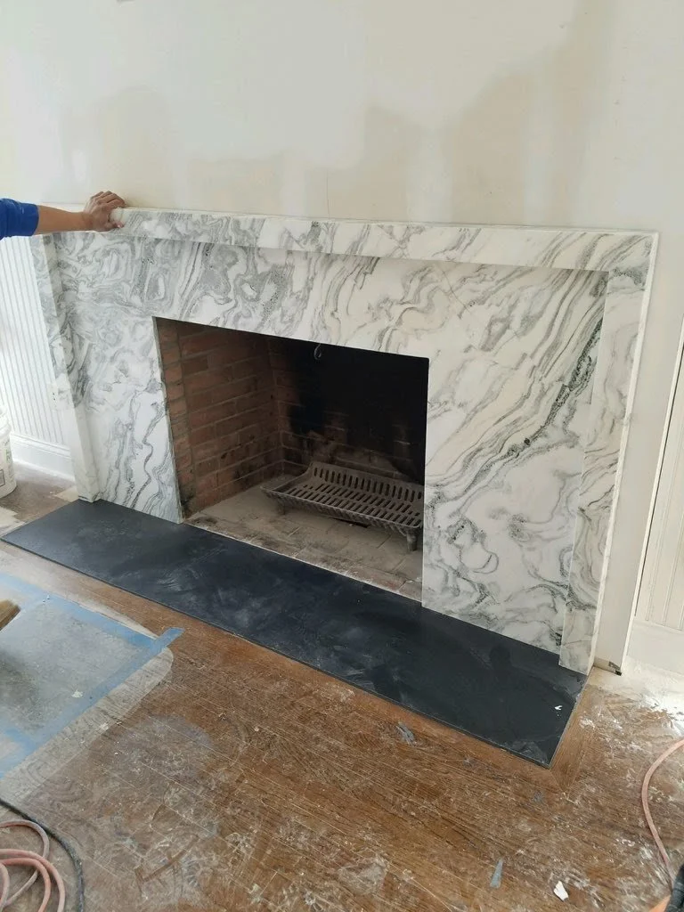 Marble fireplace surround being installed, showcasing natural stone veining and the precision required for custom interior millwork and finishes