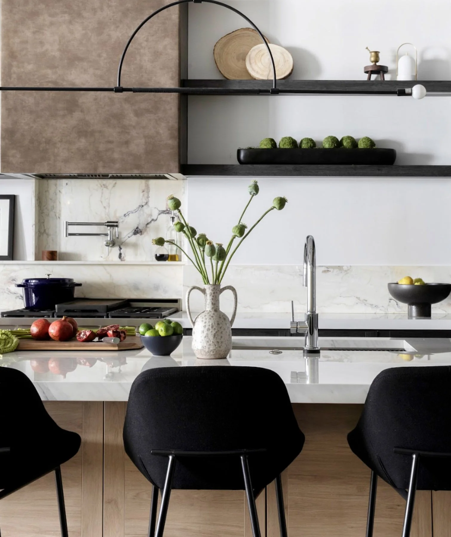 Modern kitchen with open shelves, a marble island, a vase with green flowers, and black chairs.