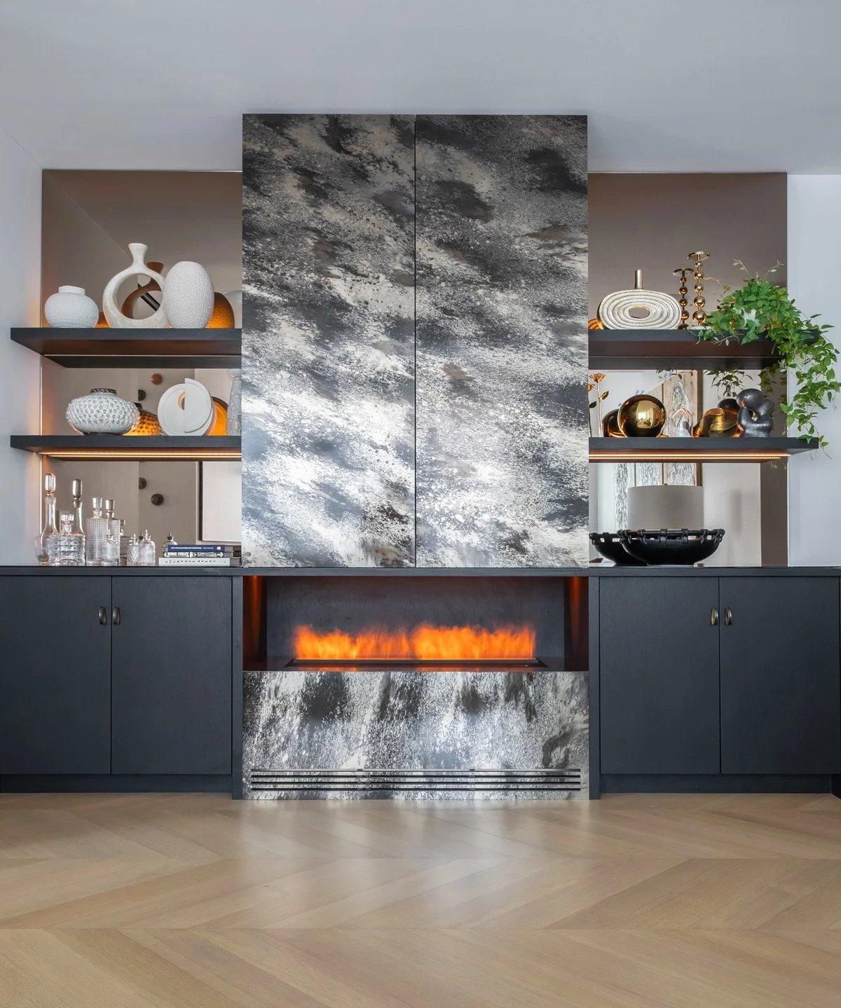 Custom millwork integrates a water vapor fireplace, home bar, and concealed storage, anchoring an underutilized area of the room. It adds warmth and balance to the floor plan without feeling added on in this Lantern House condo in Manhattan.