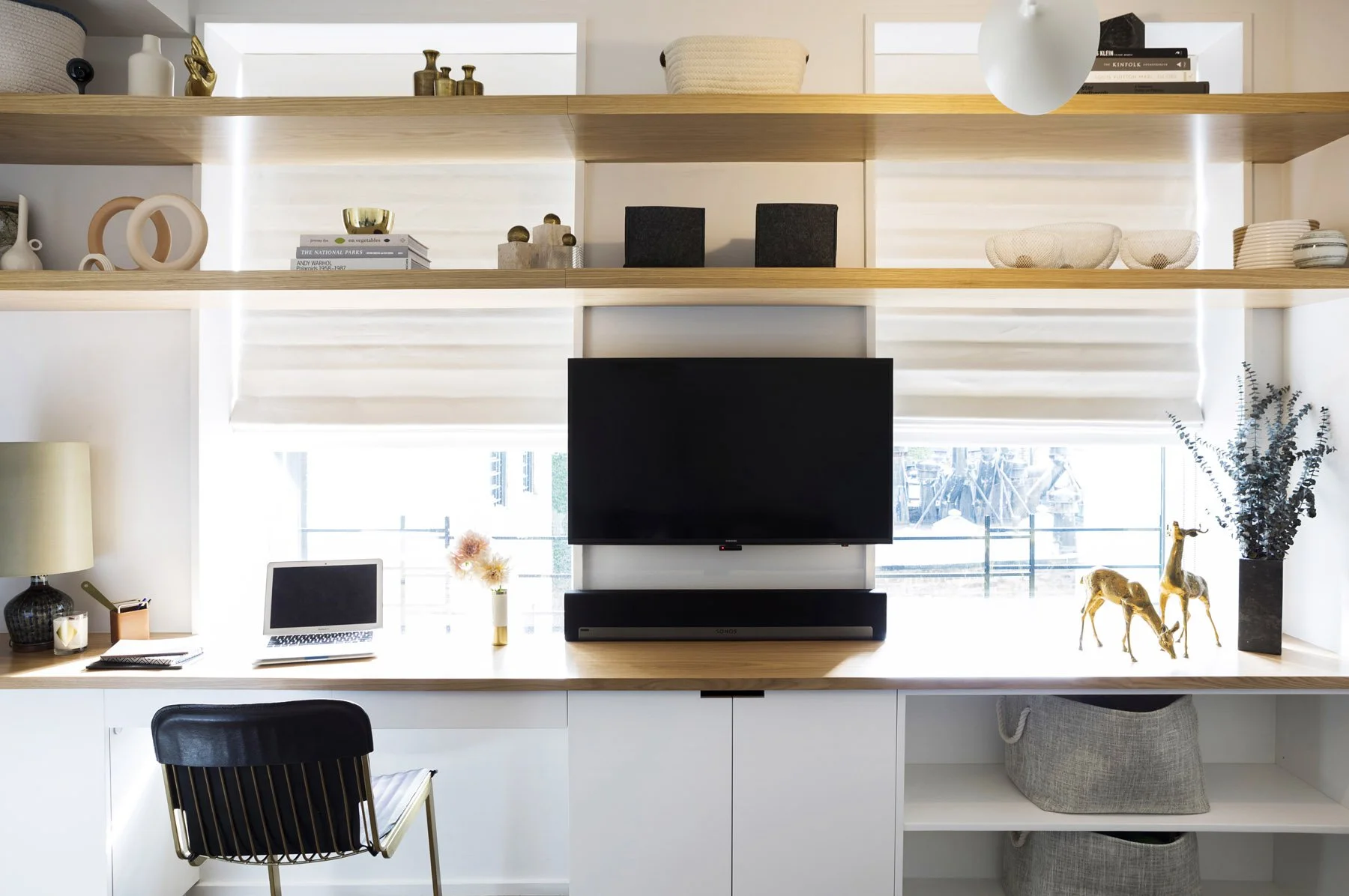 Floating custom millwork spanning the windows, with a generous work surface, discreet storage, and open display shelves. It brings order and lightness to a triple-duty room without disrupting views in the Brooklyn Heights apartment.