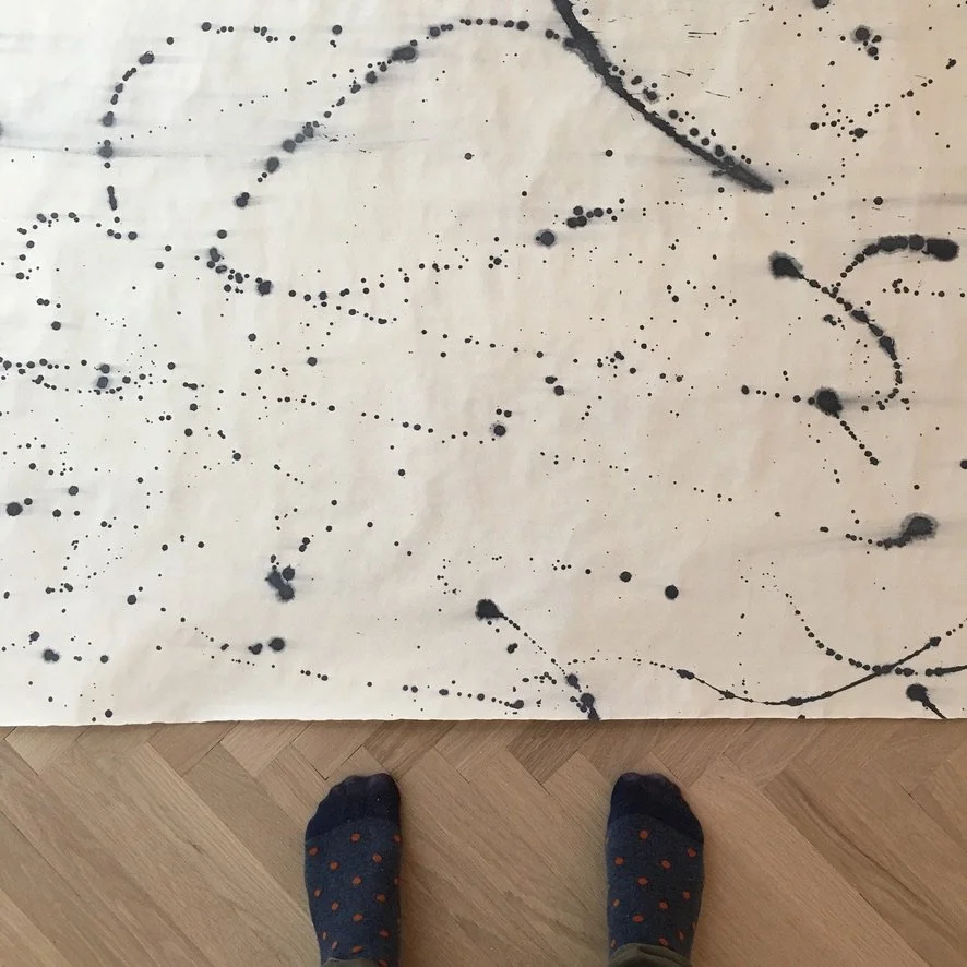 Close-up of an abstract splatter-pattern wallpaper laid over herringbone wood flooring, highlighting handcrafted detail and material texture in interior design