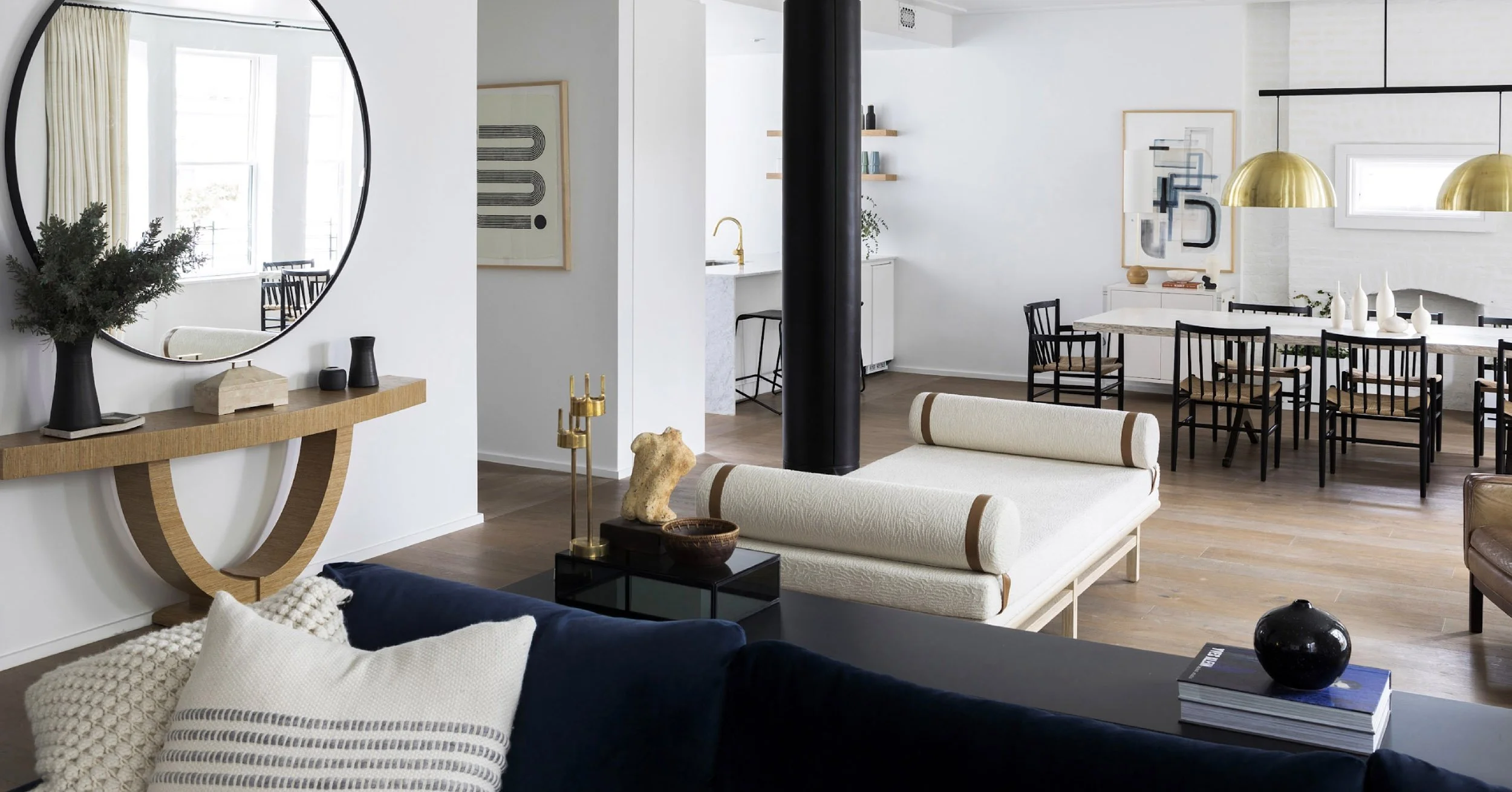 Modern open-concept living and dining area with white walls, wooden flooring, black and white furniture, gold accents, wall art, and decorative objects including vases and sculptures.