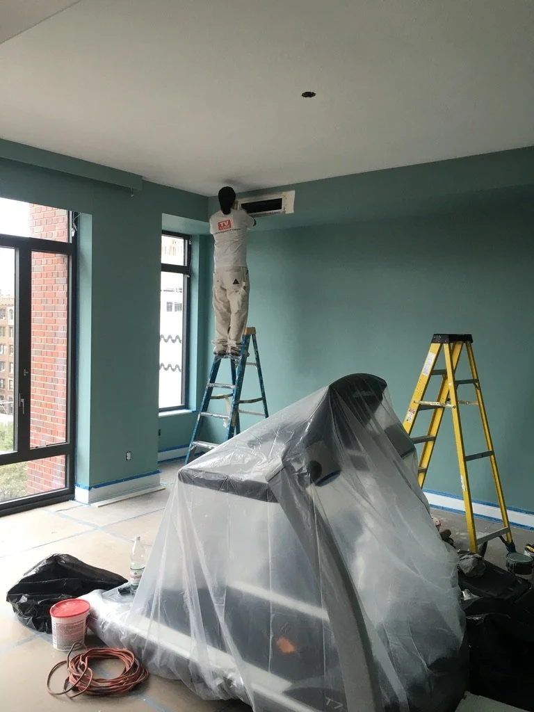 Painter on ladder applying custom wall color in a New York City apartment, showing the process and precision behind a professionally finished interior