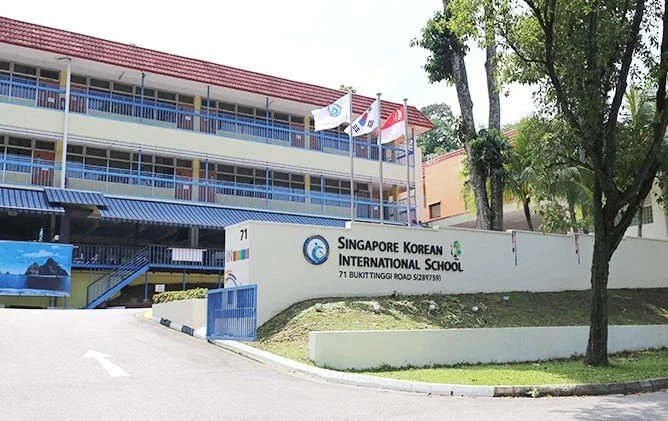 Exterior view of Singapore Korean International School with flags and signage.
