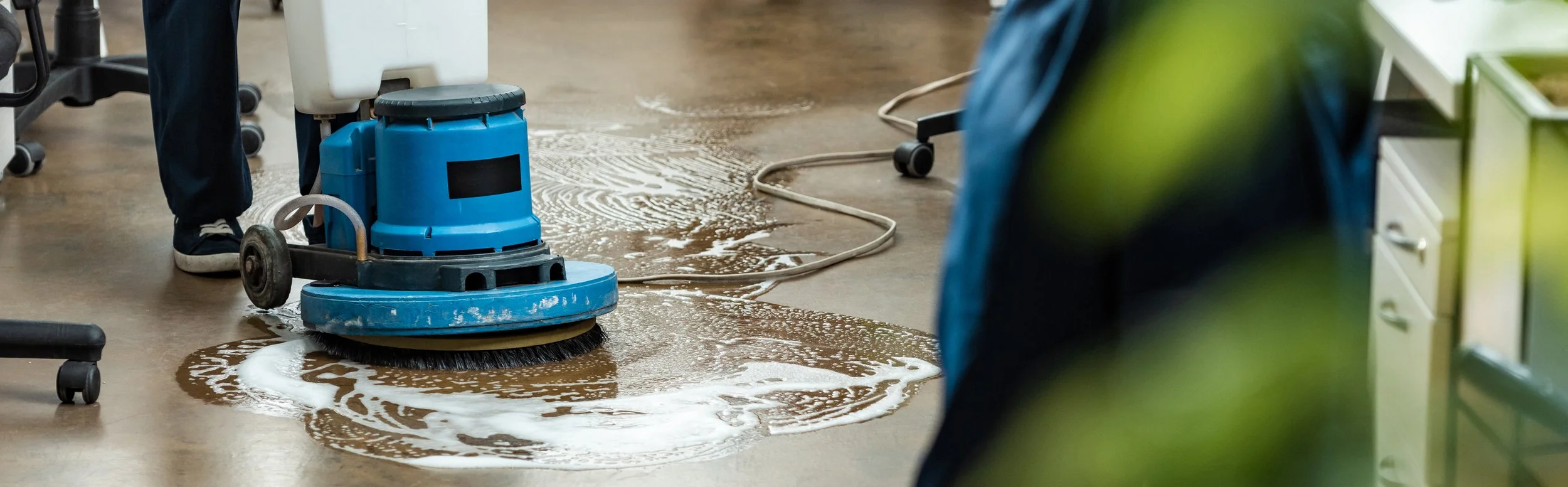 A floor cleaning machine is cleaning up a wet floor, leaving soap suds behind.