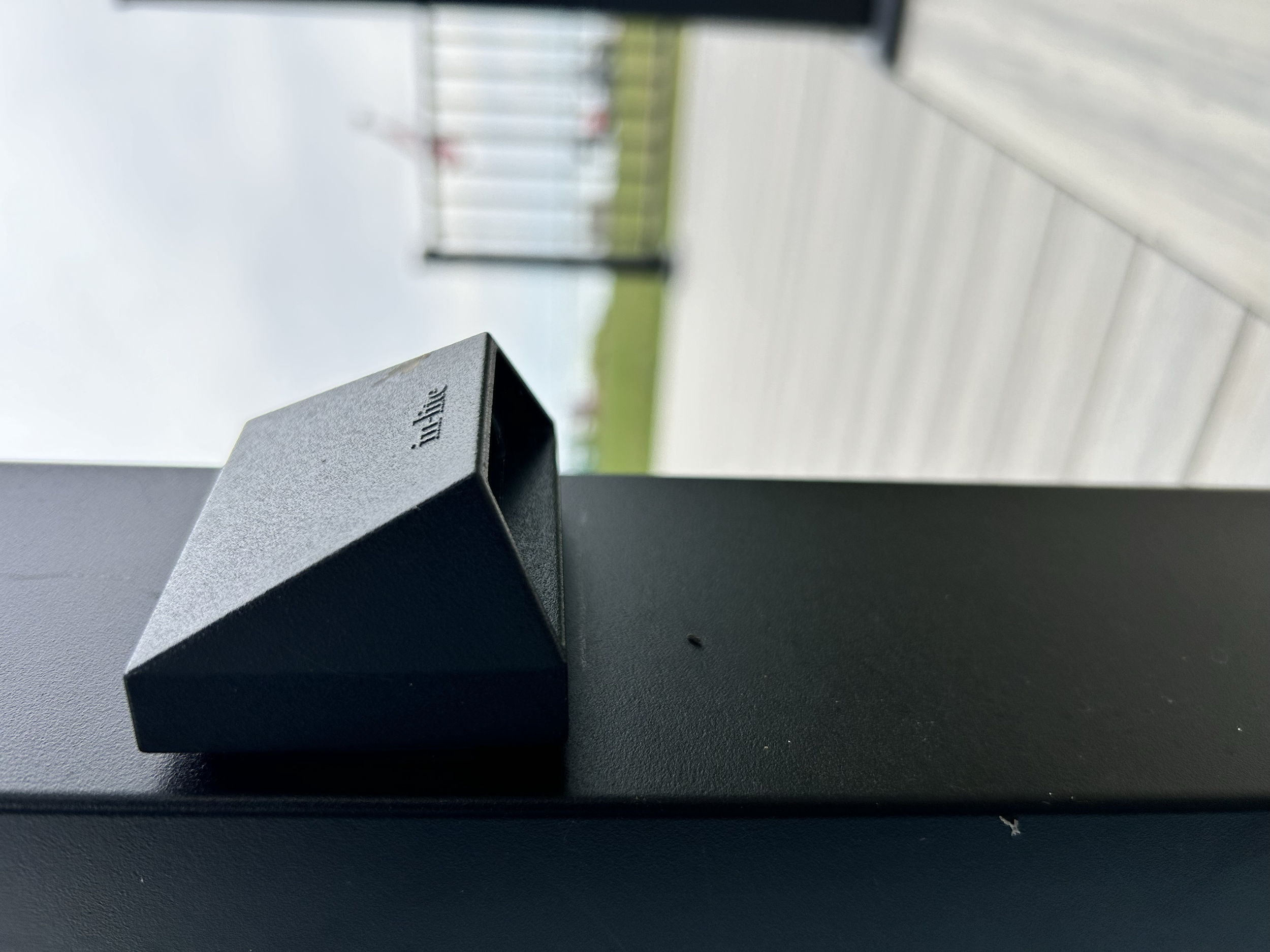 Close-up of a black mini wedge down light placed on a black surface with a body of water and a composite deck in the background.