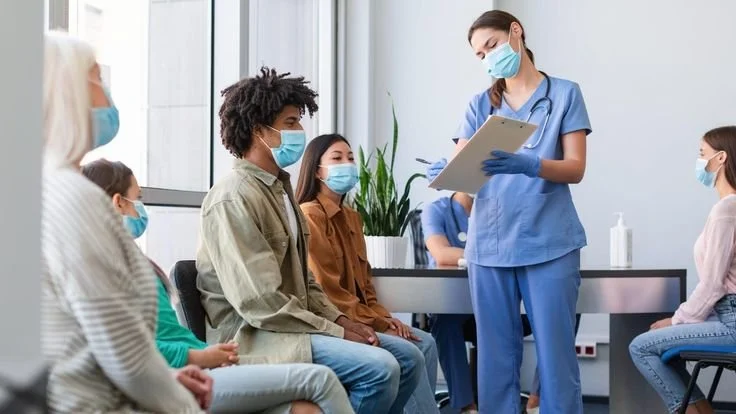 Medical professional giving a presentation to seated diverse group of patients in a clinic or hospital.