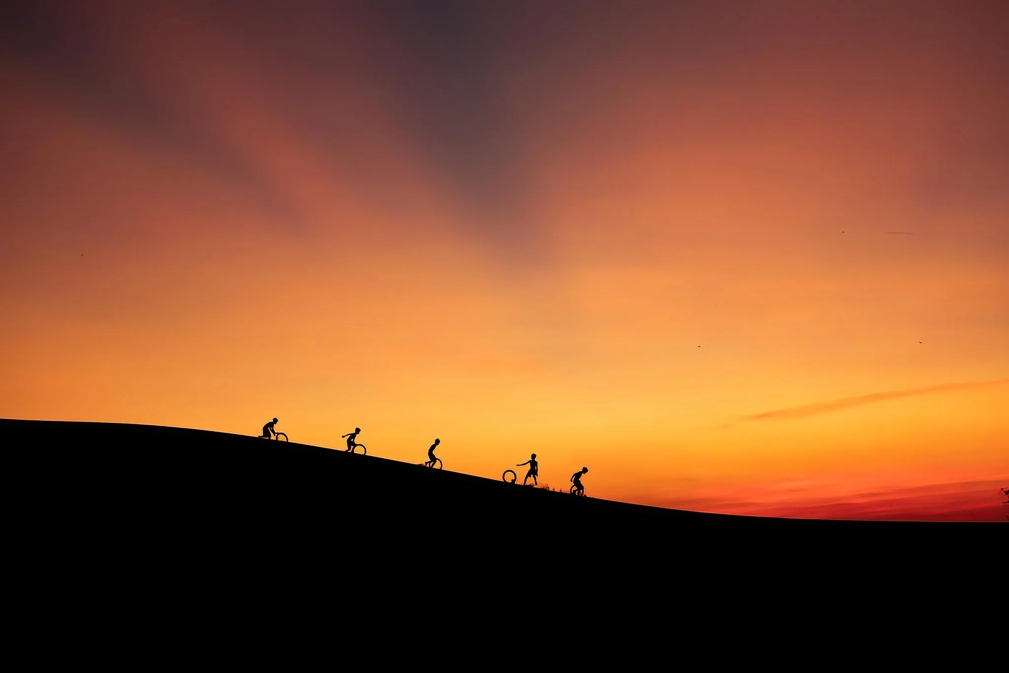Silhouettes of children playing on a hill at sunset with colorful sky in the background.