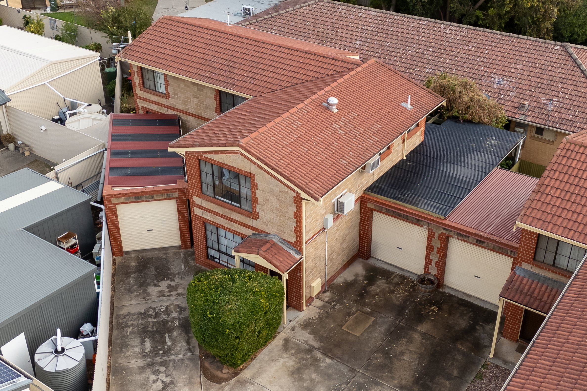 Aerial view of a residential area showing multiple houses with tiled roofs, a small tree, and some sheds with metal roofs.