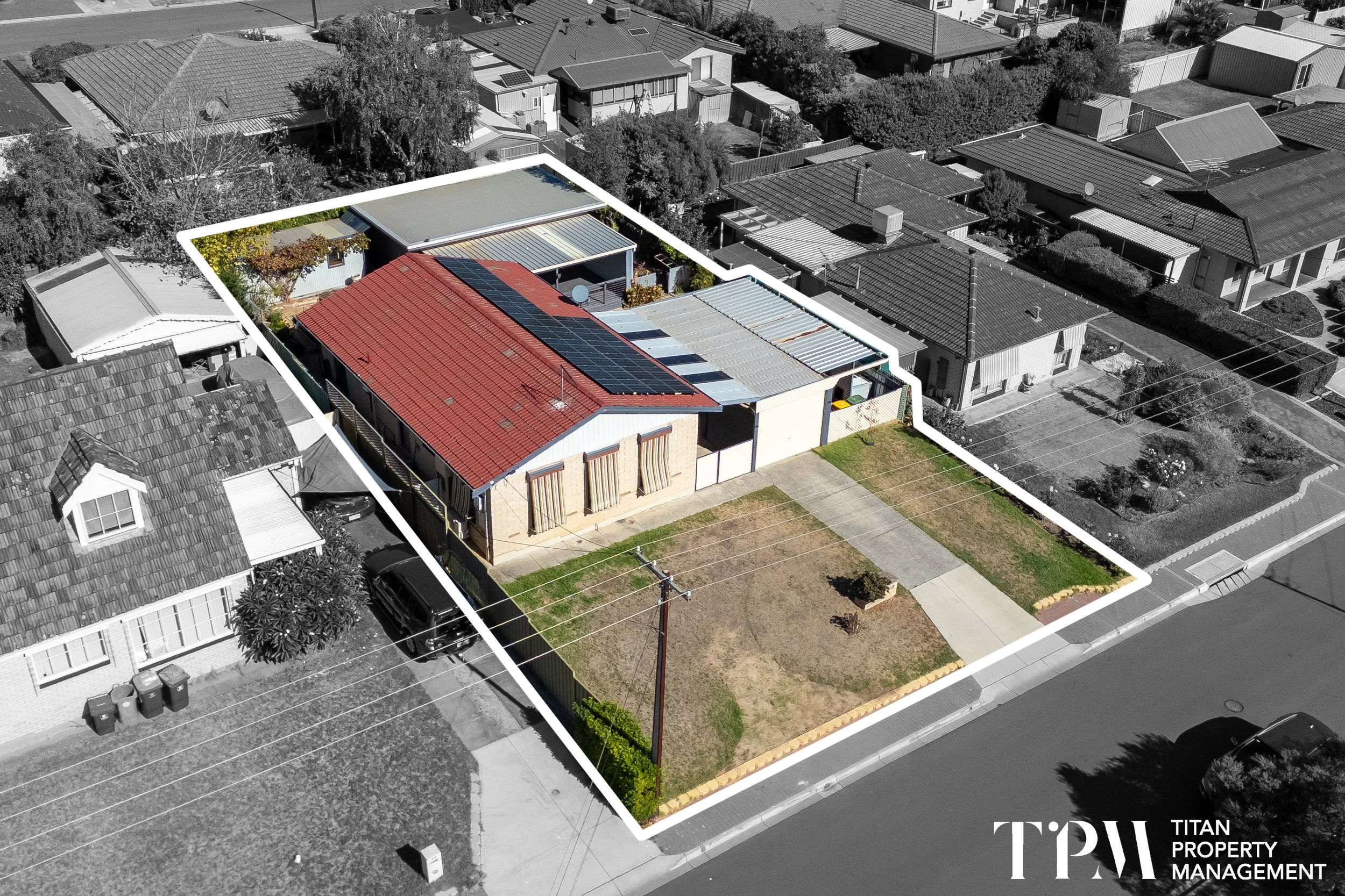 Aerial view of a residential neighborhood with one house outlined in white, featuring a red roof with solar panels and a backyard with green grass and plants, in black and white with color highlighting the outlined house.