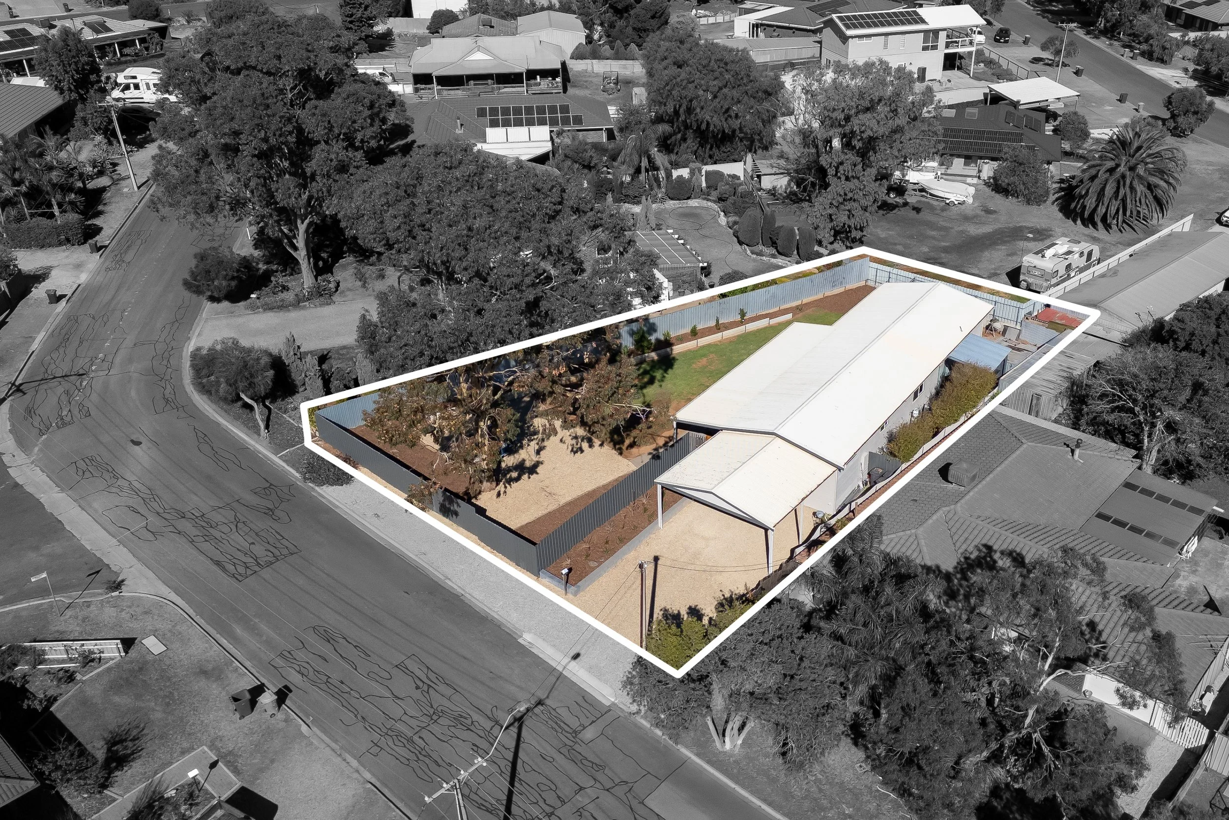 Aerial view of a residential neighborhood with a highlighted backyard that includes a lawn, trees, and a fence, surrounded by houses, trees, and parked vehicles.