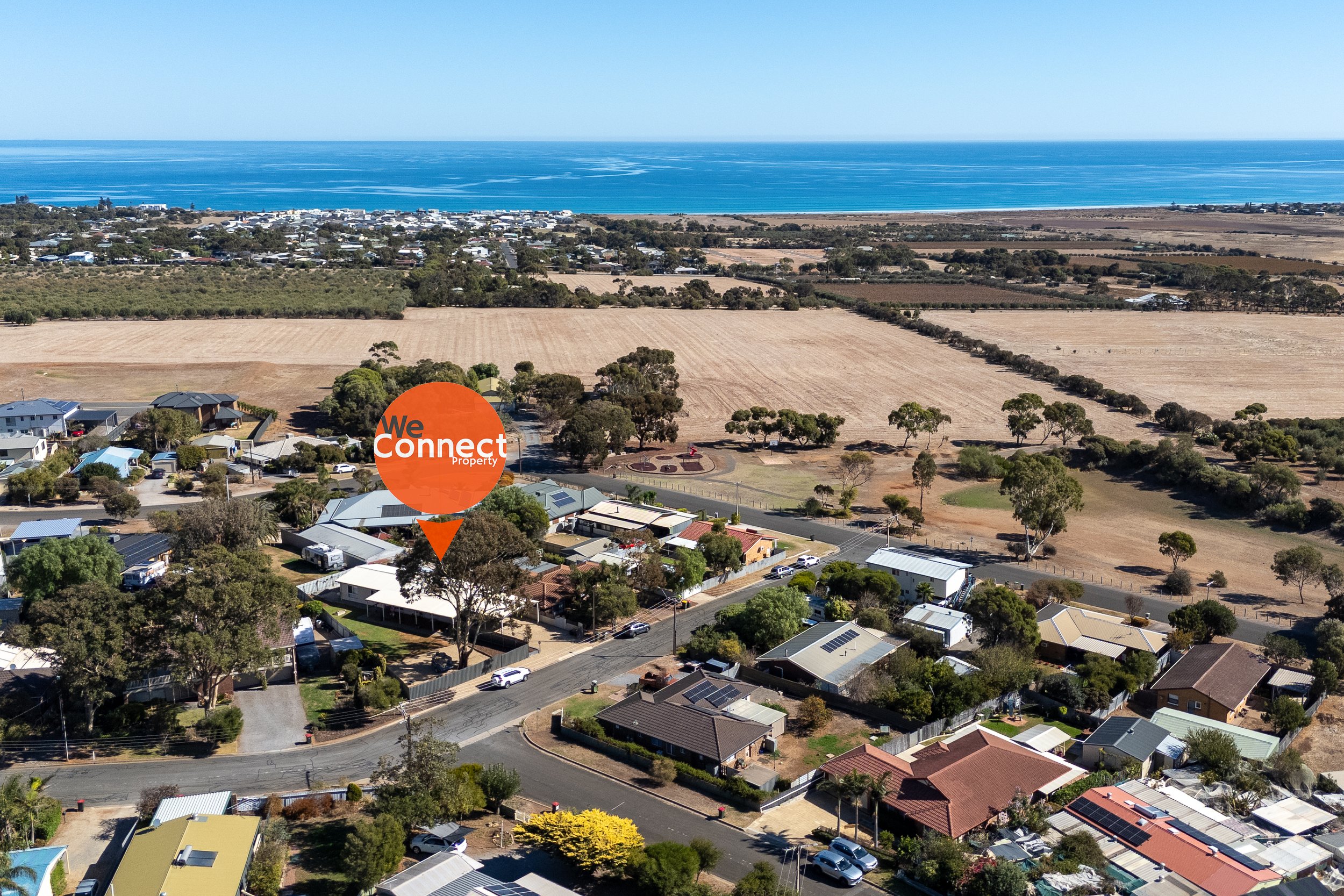 Aerial view of a coastal town with houses, trees, and open fields near the ocean, with a 