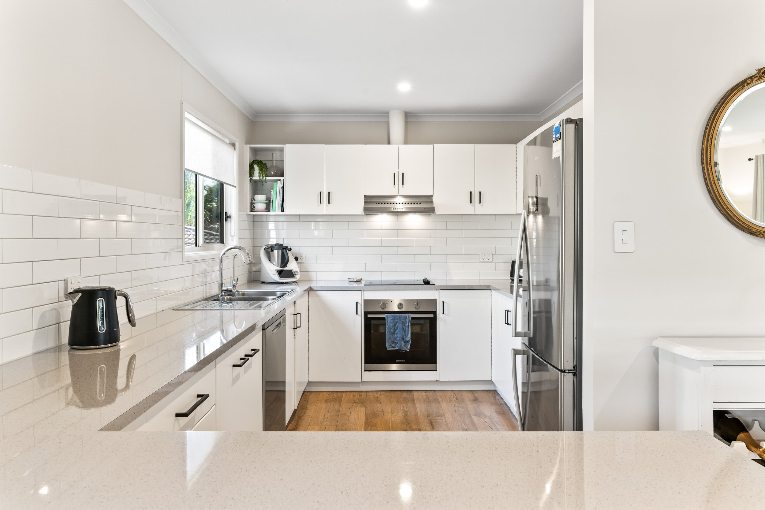 Clean modern kitchen with white cabinets, stainless steel appliances, a white tiled backsplash, and wooden flooring.