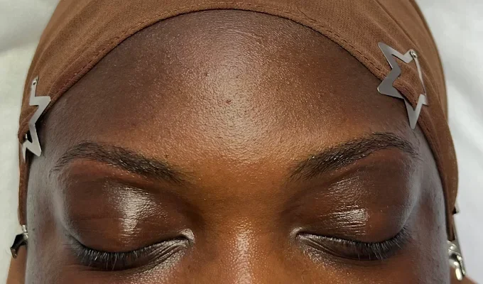 Close-up of a person's forehead with two star-shaped hair clips, eyes closed, and wearing a brown head covering.