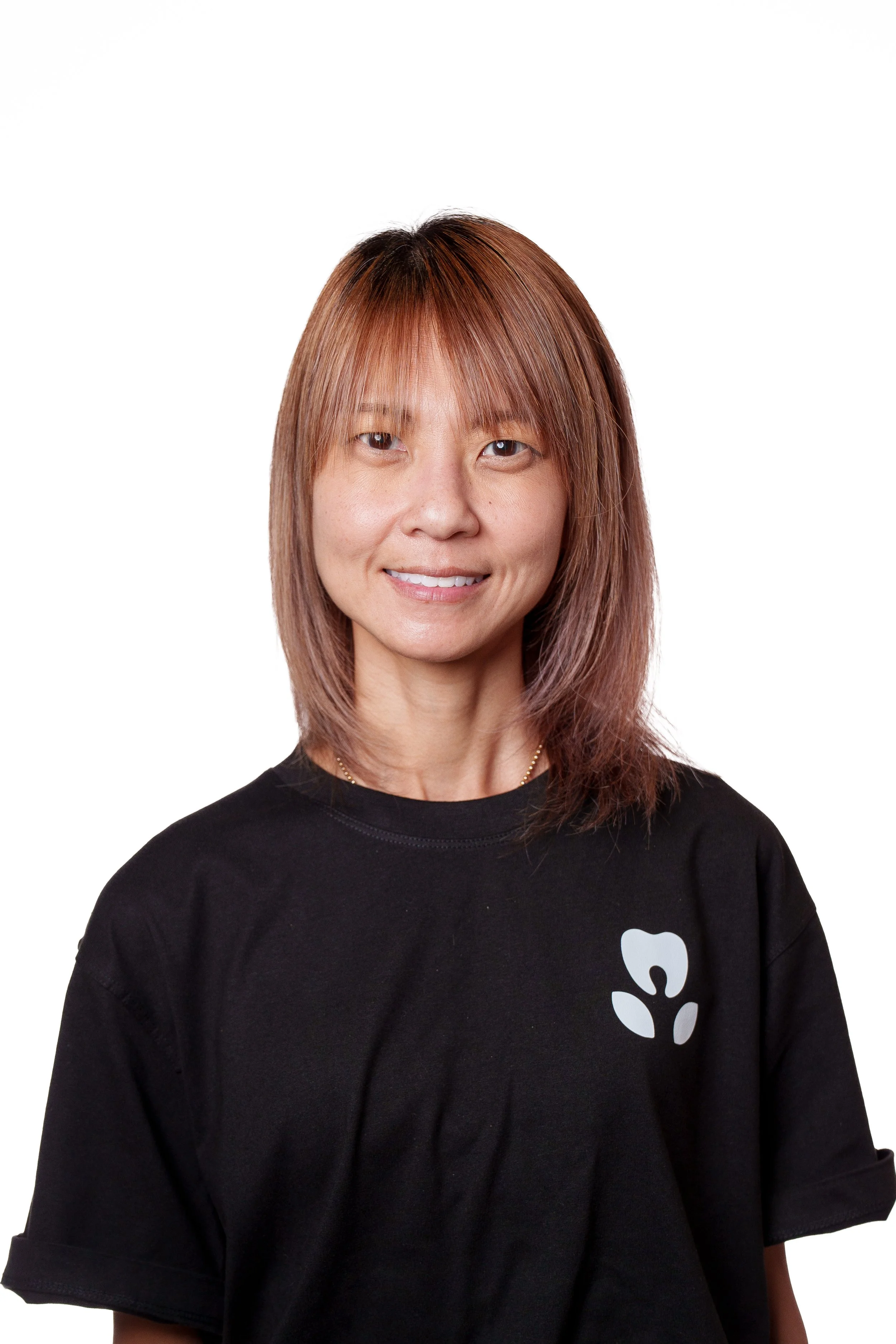 A woman with shoulder-length light brown hair with reddish highlights, smiling slightly, wearing a black t-shirt with a minimalist white logo of a paw print on the front, against a plain white background.