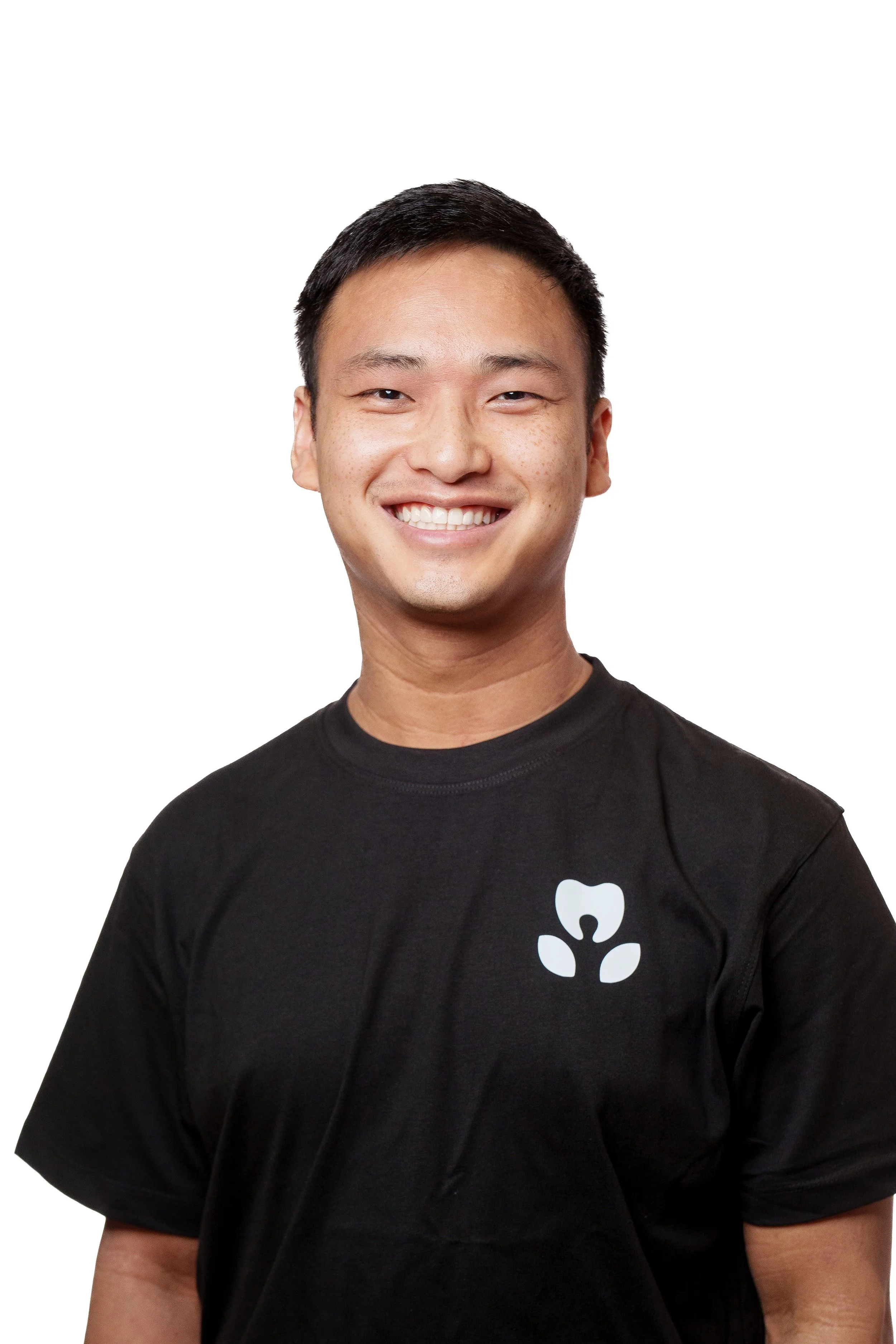 A young man with short black hair and a bright smile, wearing a black t-shirt with a white logo on the chest, against a plain white background.