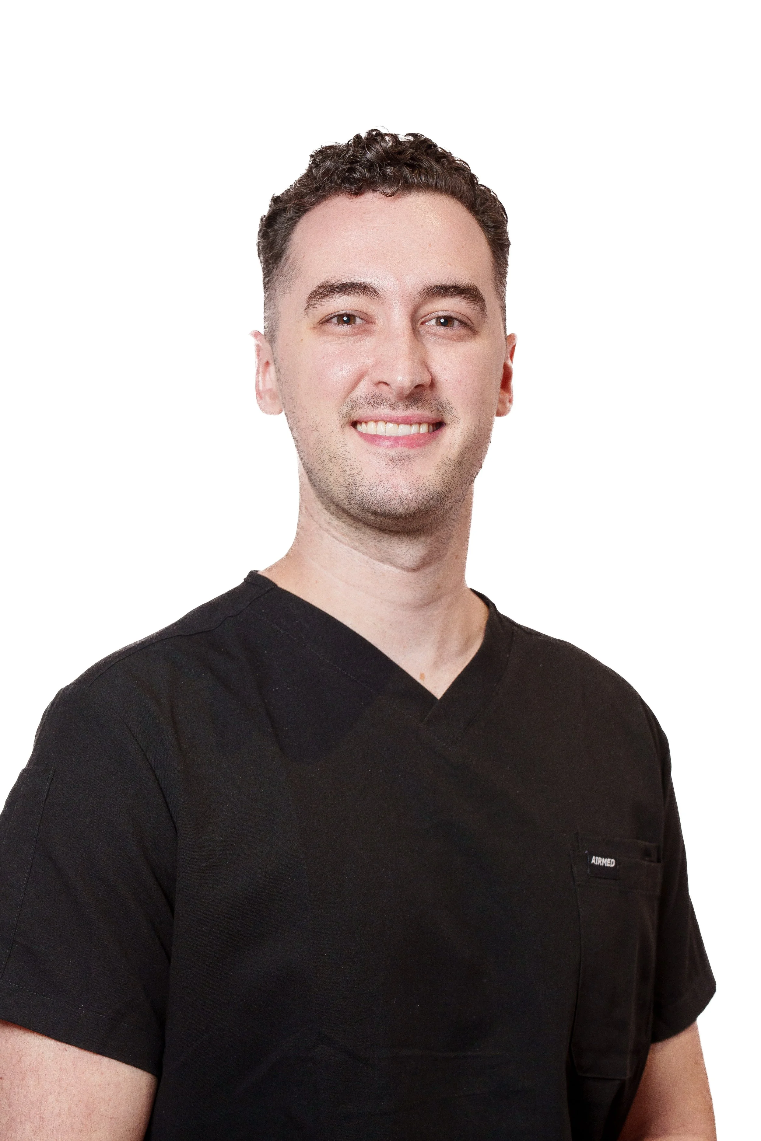 A smiling young man wearing a black medical scrub top with a small pocket on the left side, standing against a white background.