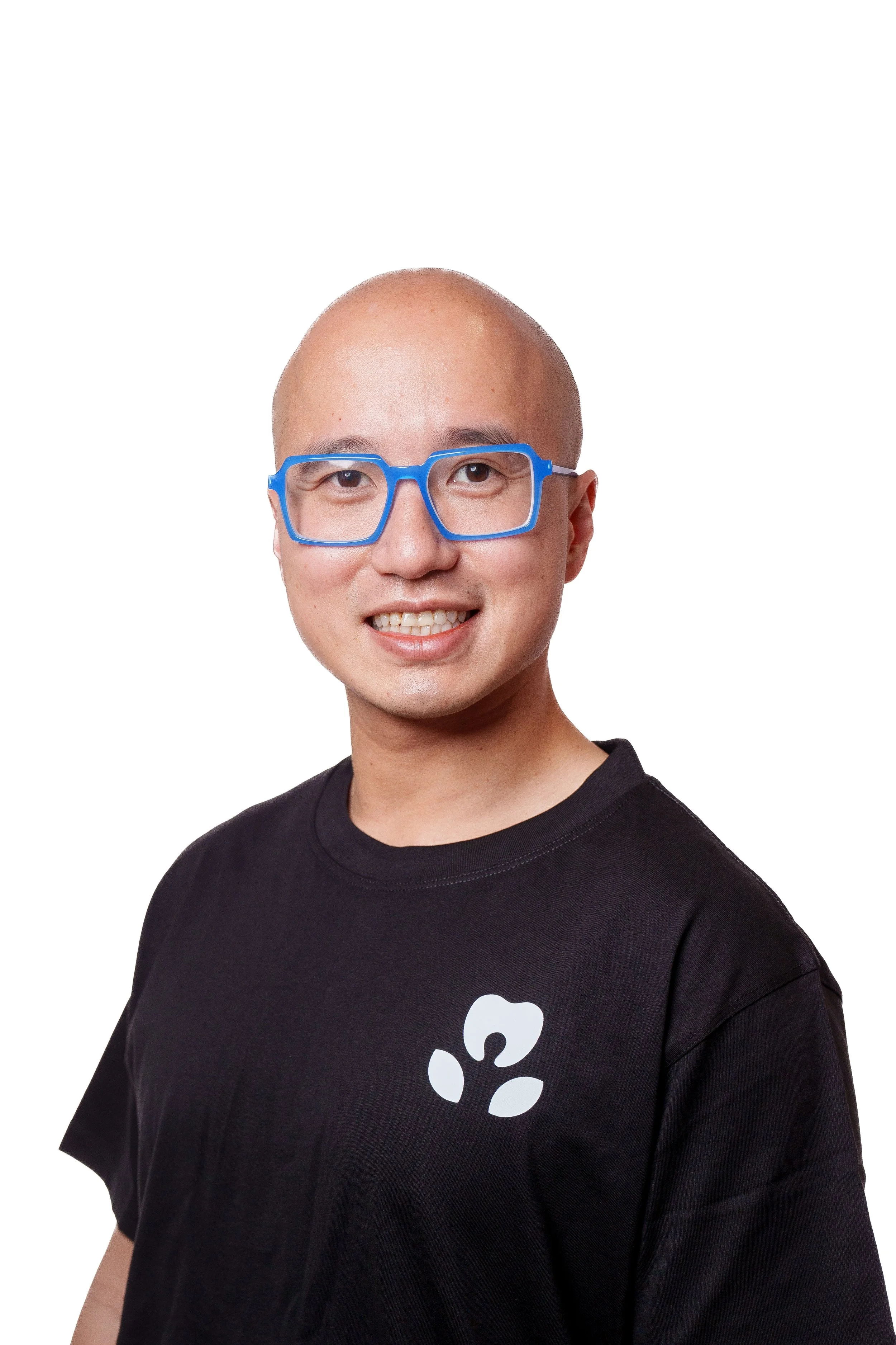 A young man with a shaved head wearing blue glasses and a black T-shirt with a white paw print logo.