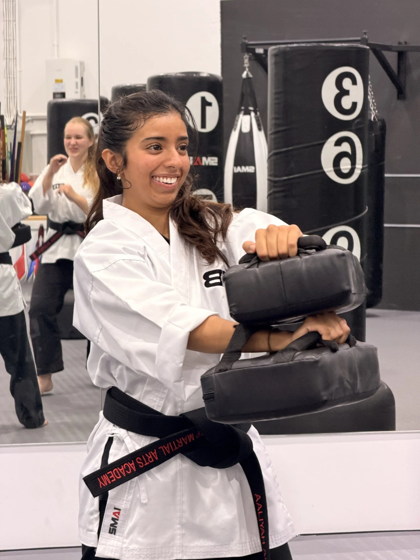 A man with dark, curly hair, glasses, and a beard looks slightly to the side. He's wearing a dark sweater and is indoors with a blurred plant in the background.