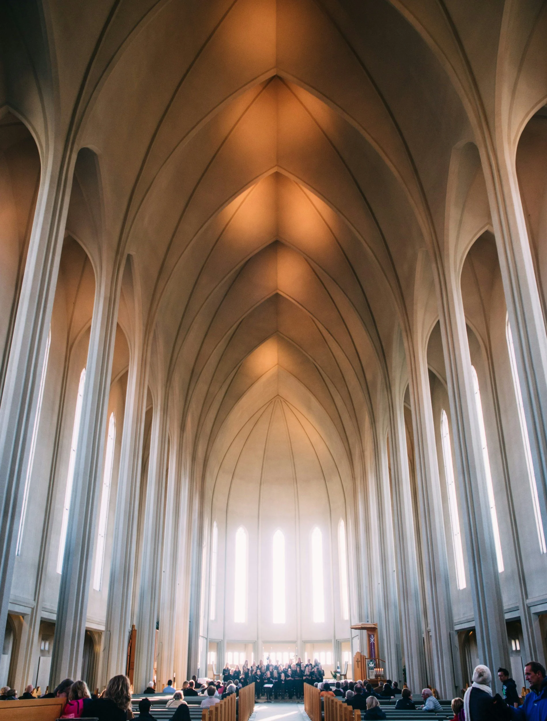 Interior view of a large church with high vaulted ceilings and rows of pews filled with people attending a service or event.