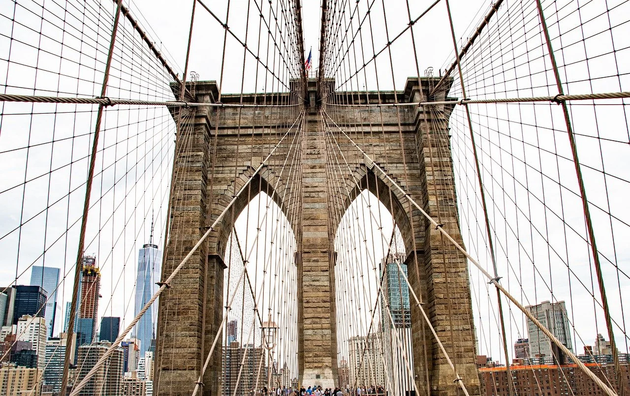 View of Brooklyn Bridge with its stone towers and suspension cables, looking towards Manhattan skyline with skyscrapers