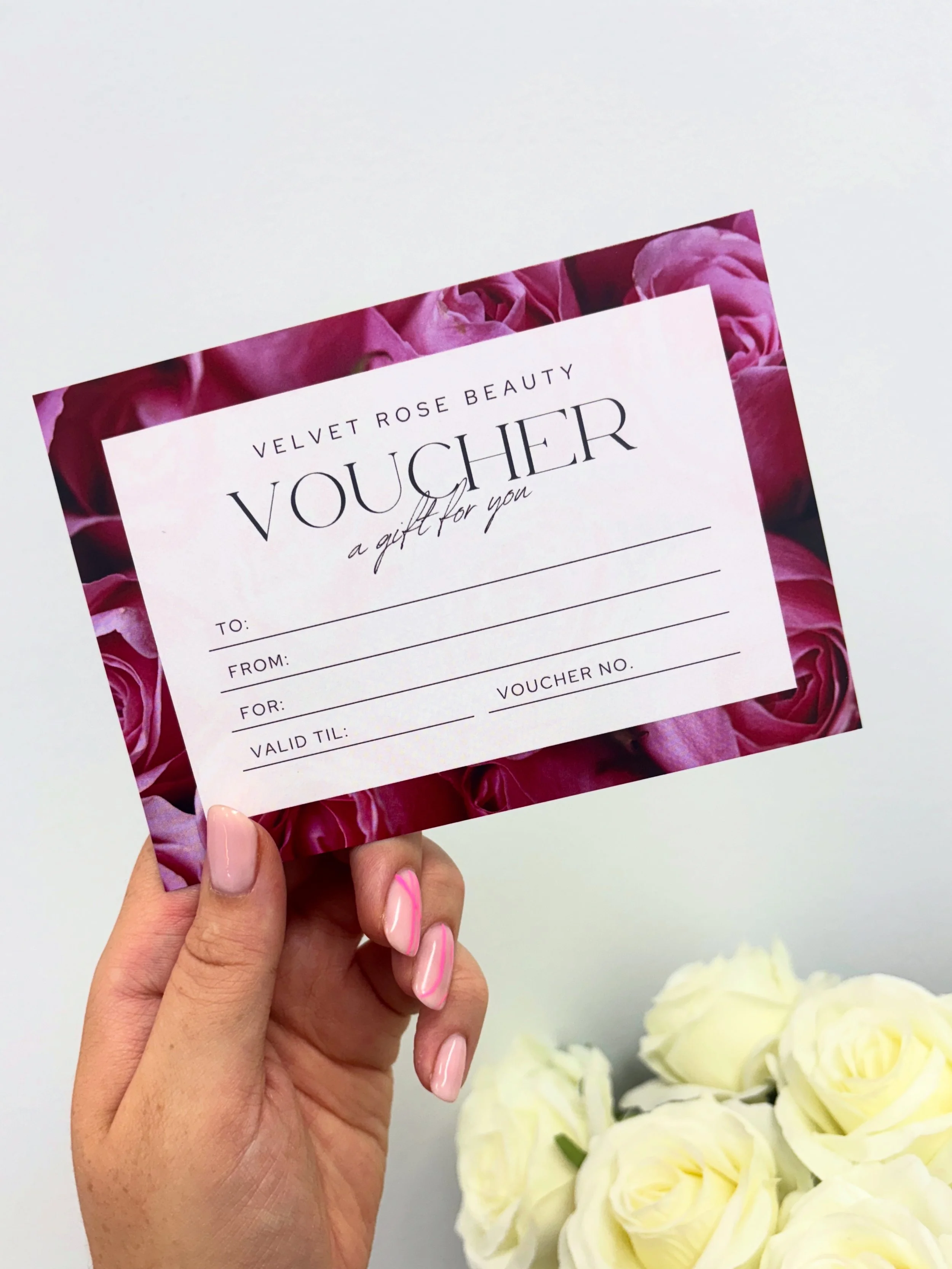 Person holding a pink and white voucher with pink roses border, with white roses in the background.