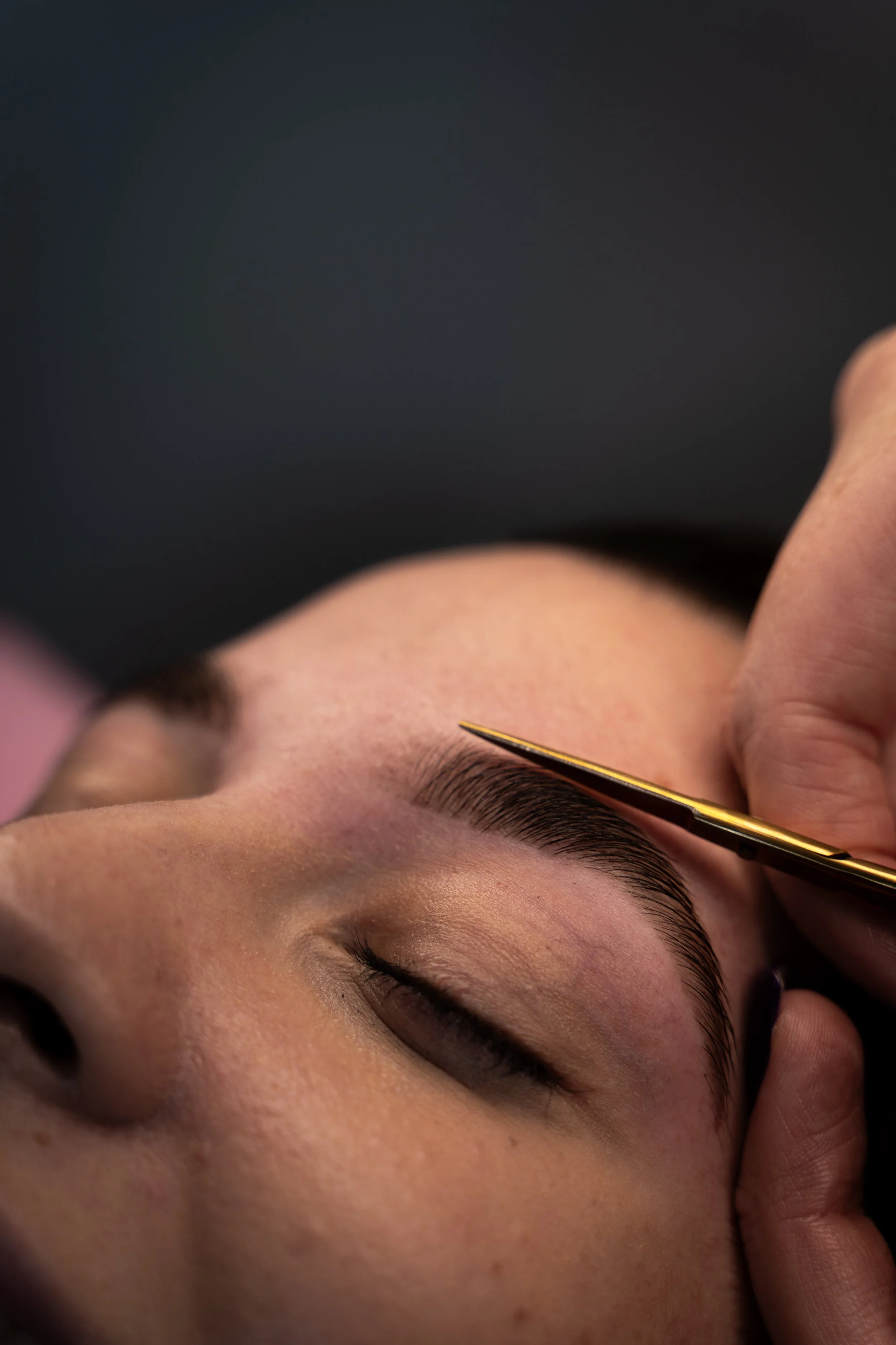 A young woman is lying down having her eyebrows shaped and tinted in Perth