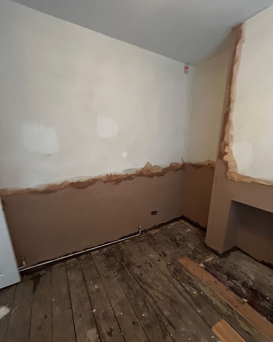 Room in the process of renovation with partially removed wall paneling and damaged hardwood floor.