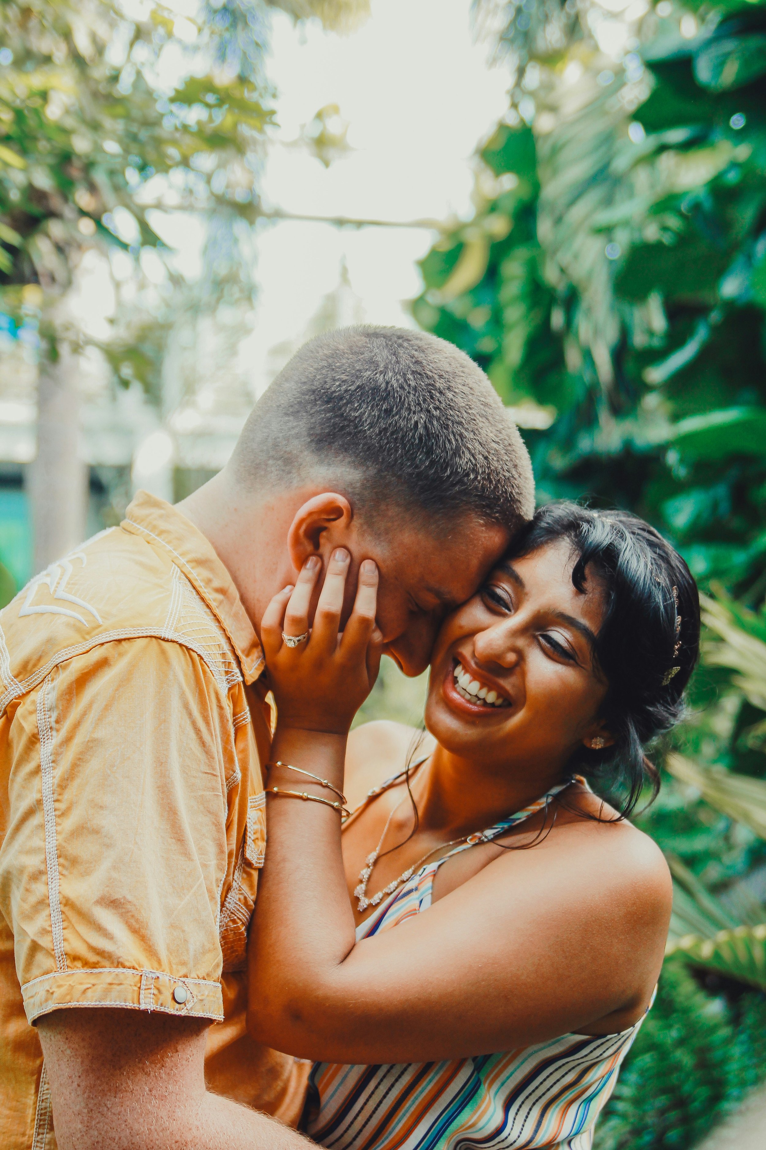 A couple sharing a joyful moment outdoors, with the woman touching the man's face and both smiling.