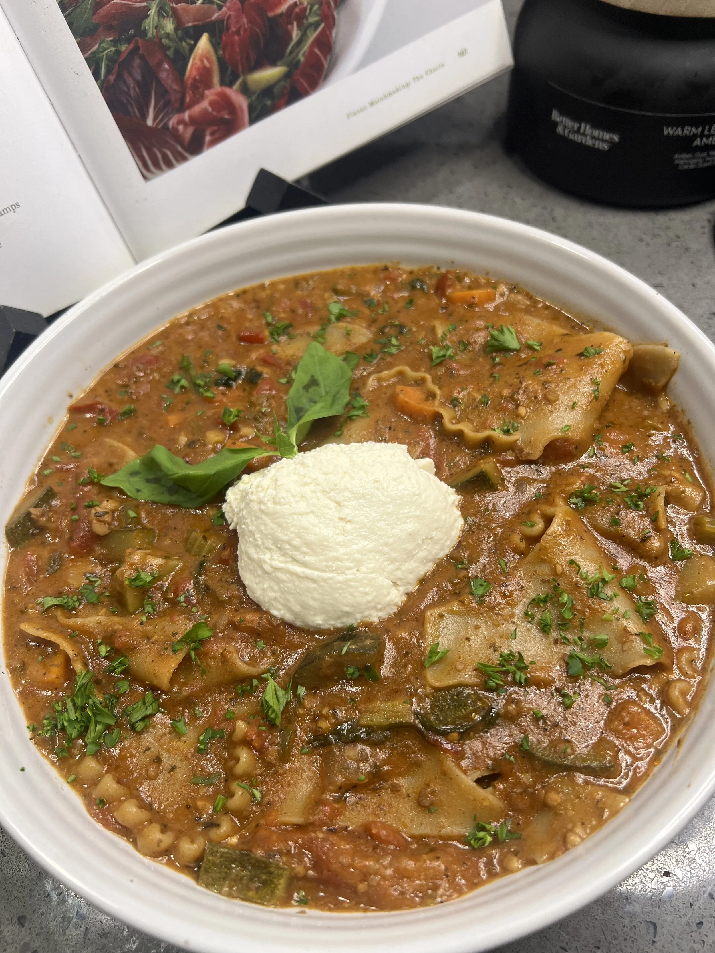 Bowl of hearty stew topped with a scoop of sour cream and garnished with fresh basil and chopped parsley.