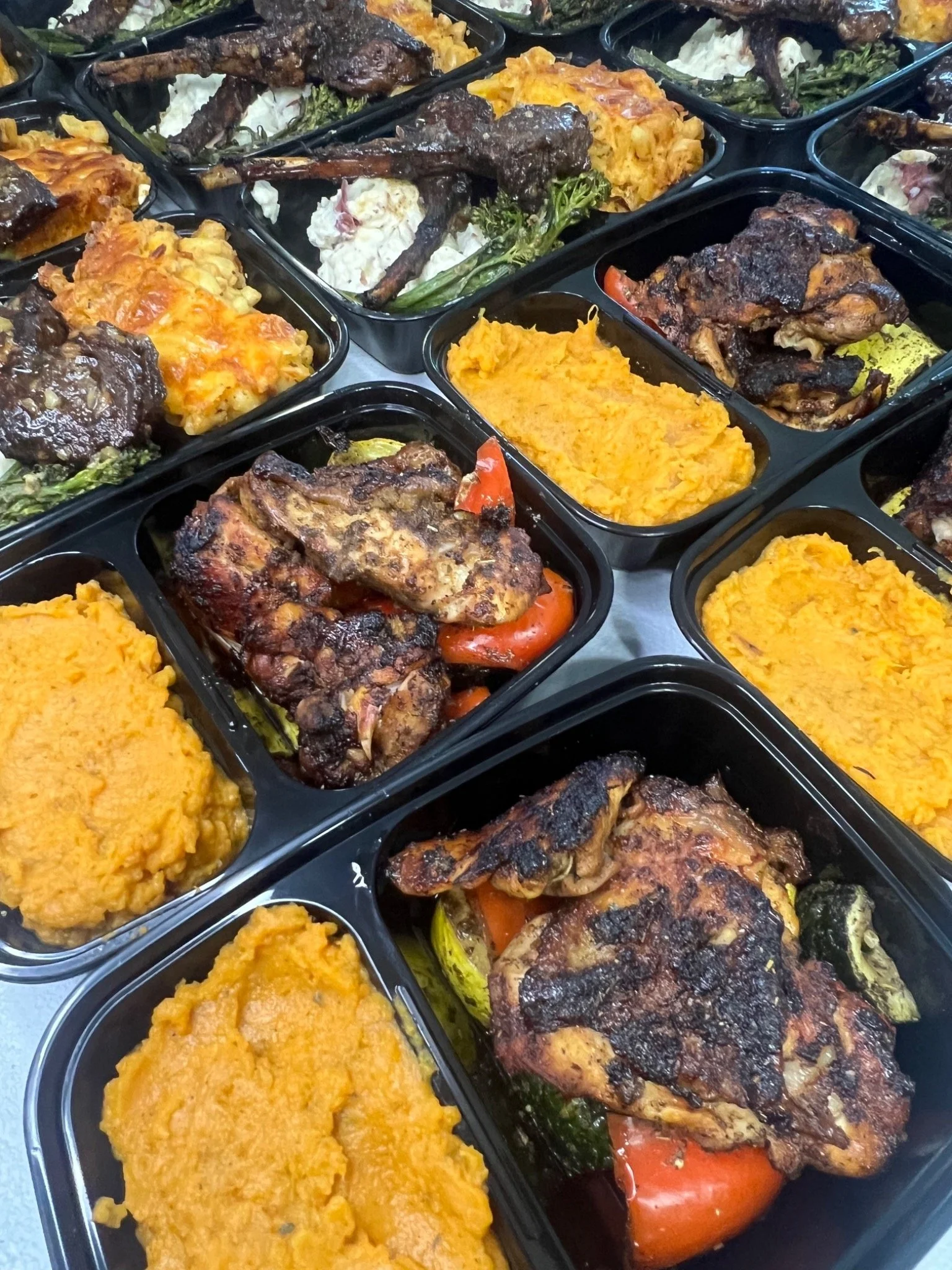 Multiple meal prep containers filled with baked chicken, sweet potato mash, roasted vegetables, and macaroni and cheese.