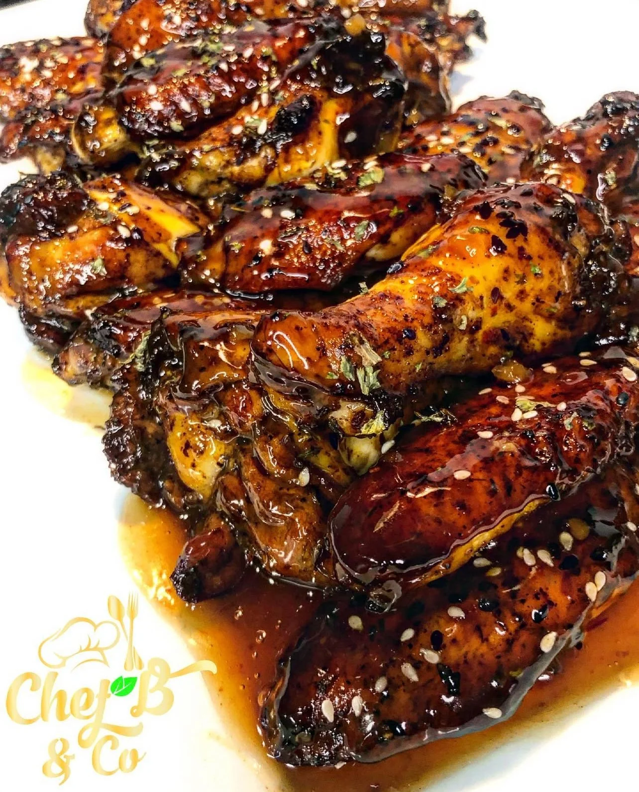 Close-up of grilled chicken drumsticks covered in barbecue sauce topped with sesame seeds and herbs.