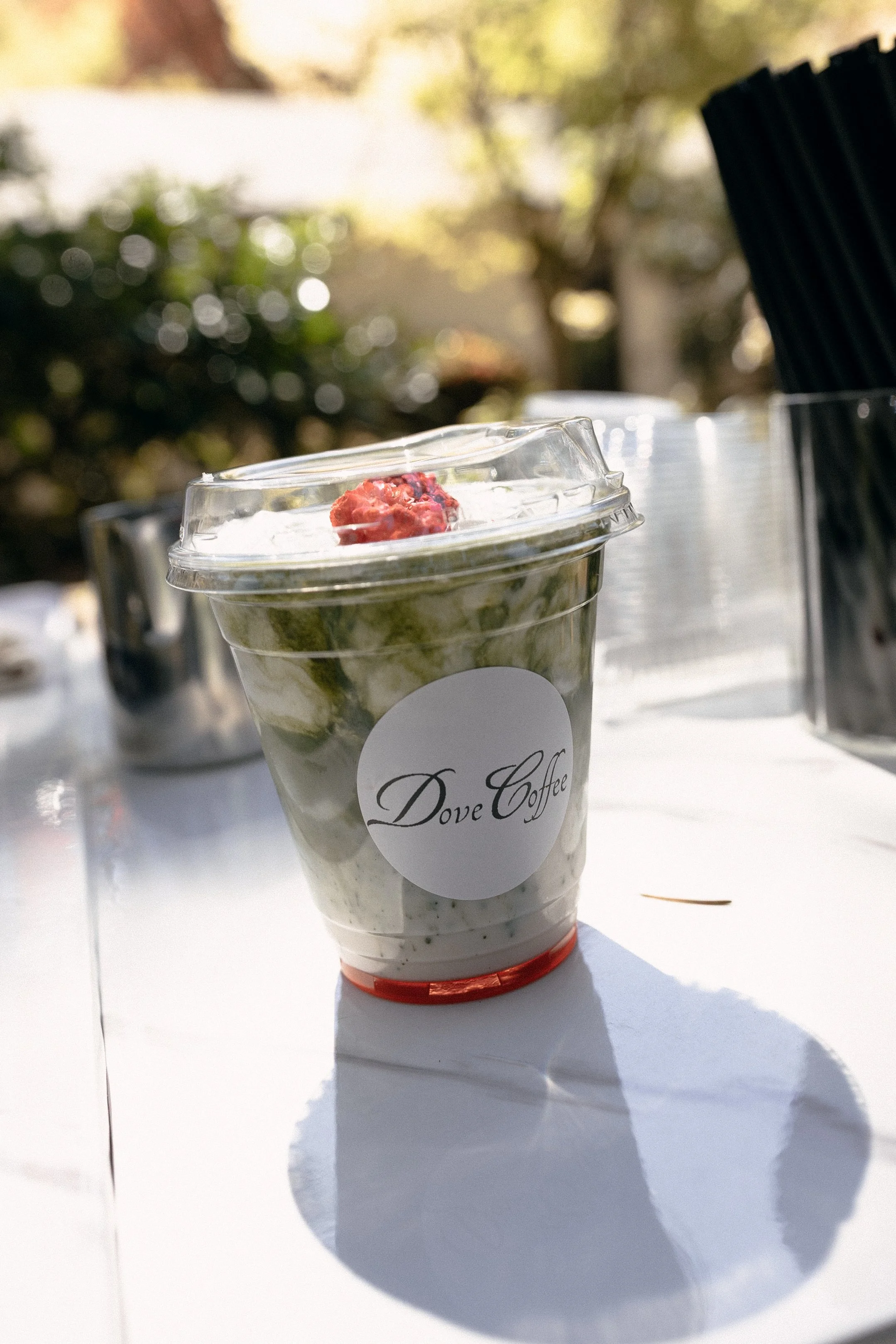 Clear plastic cup of ice cream with a label that says Dove Coffee on it, placed on a white surface outdoors, with a blurry background and a shadow cast on the surface.