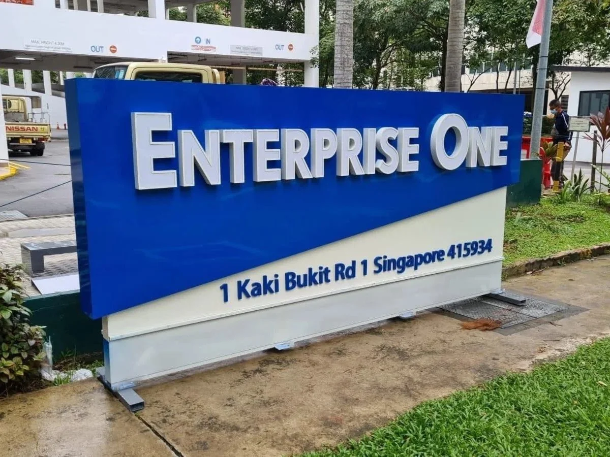 Sign for Enterprise One with address 1 Kaki Bukit Rd 1 Singapore 415934, outdoors with greenery and trees in the background.