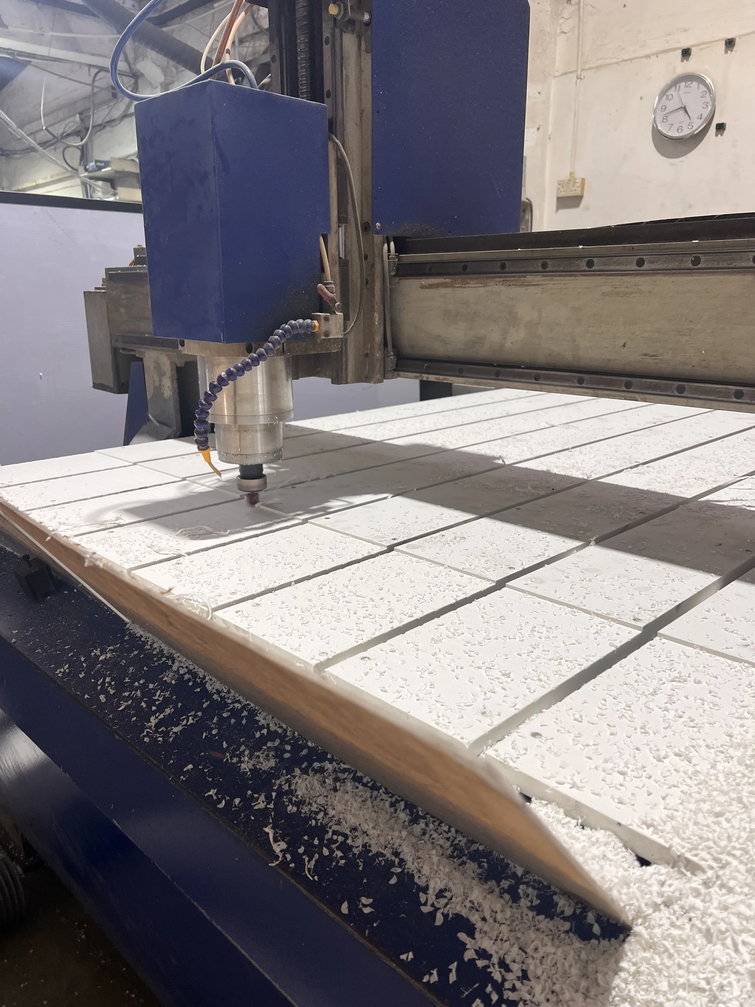 A CNC machine cutting white material, possibly stone or foam, with chips scattered on the table.