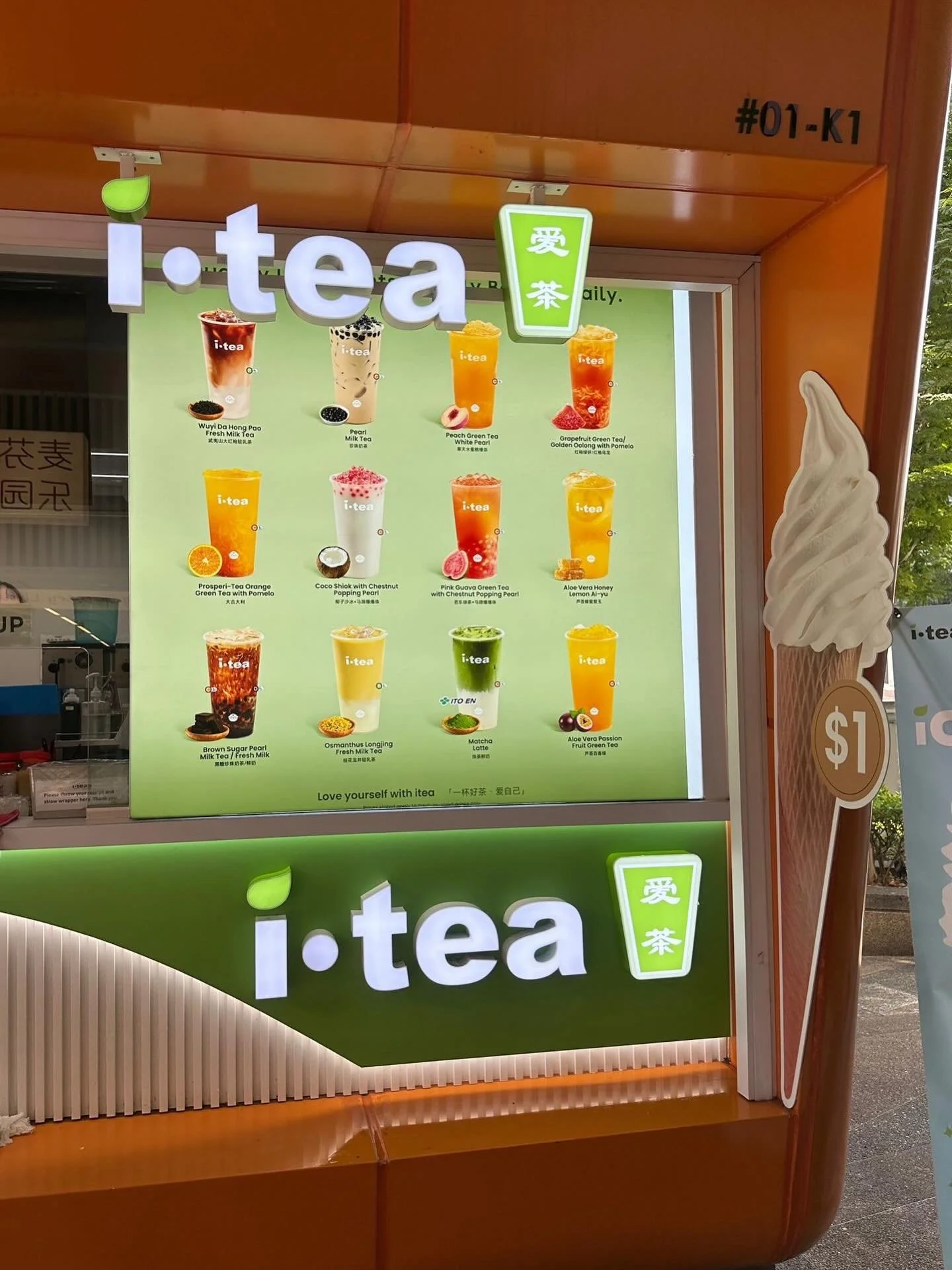 A menu board for i-tea featuring various bubble tea drinks with colorful pictures and descriptions, positioned outside on a bright day.