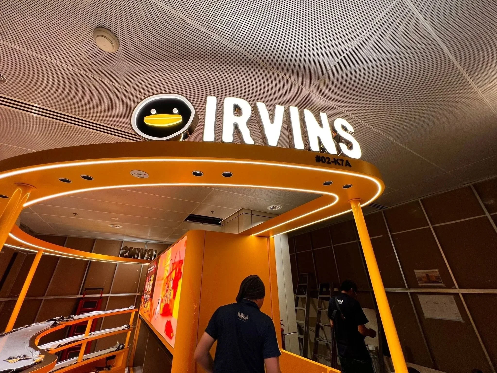 Sign for Travis with illuminated letters and a cartoon duck face logo on the ceiling above.