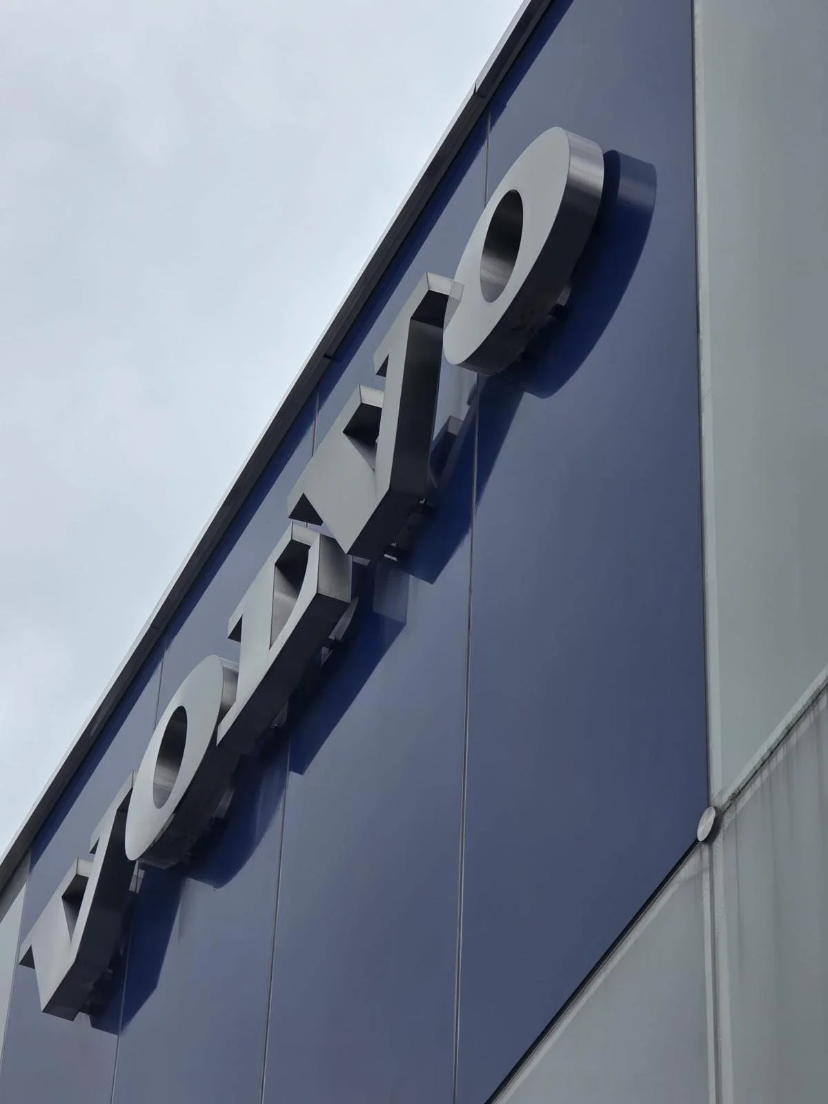 Close-up of a blue building facade with a metallic sign spelling out the word 'TOYO' mounted at an angle.