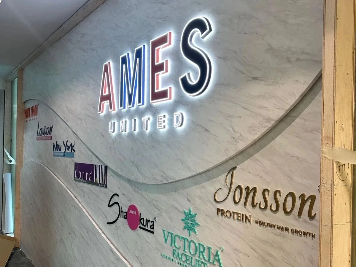 Logo wall with the large illuminated text 'AMES UNITED' and various other smaller brand names and logos, including Jonsson, Victoria, and others, on a marble-like wall with a wooden frame on the right side.
