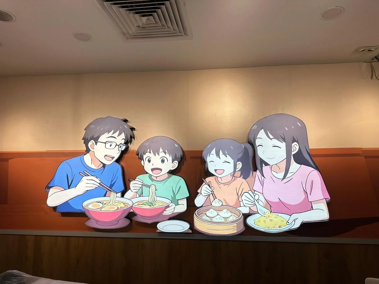 Illustrated family of five enjoying a meal together at a restaurant, with ramen, dumplings, and noodles on the table.