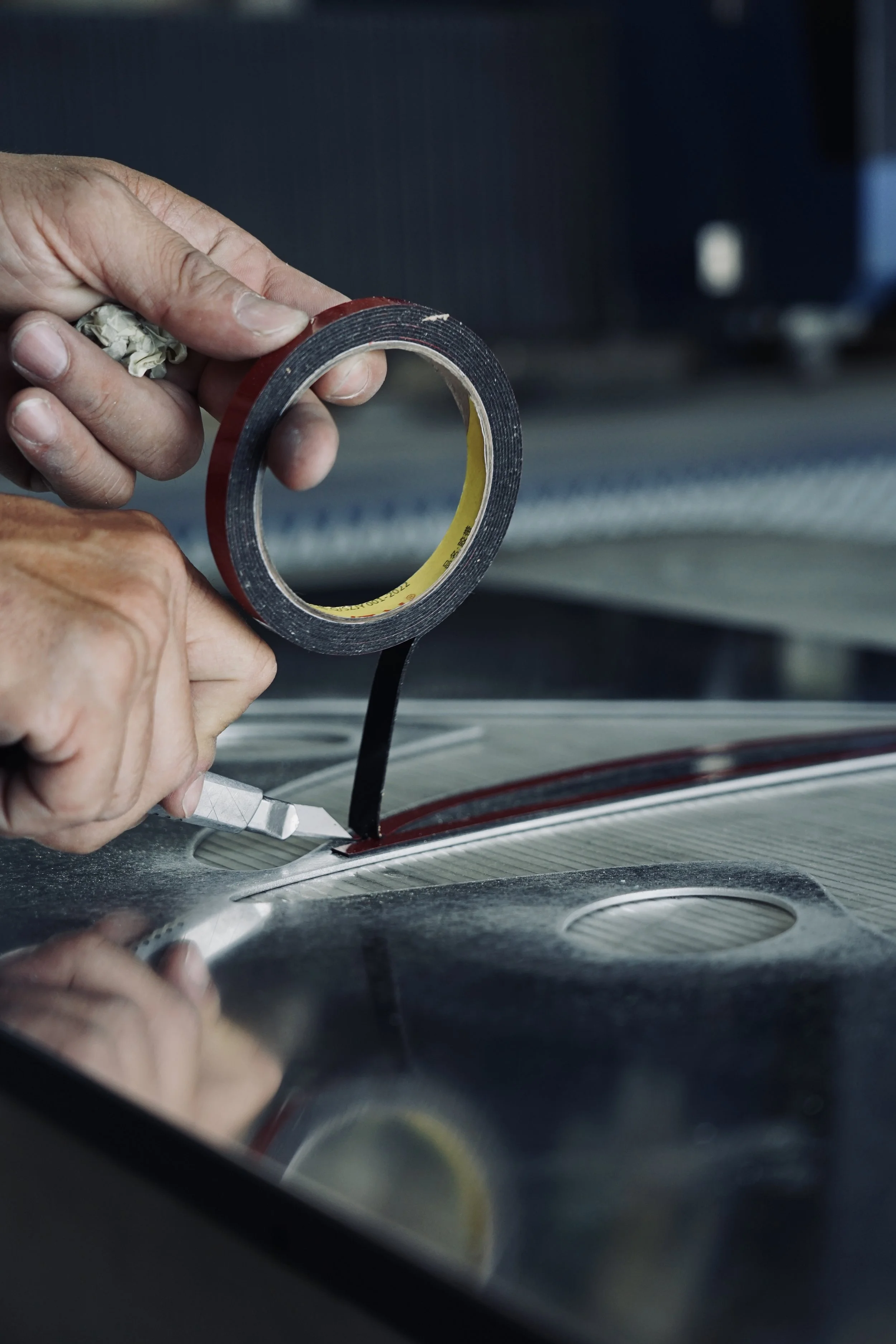 A person is using a utility knife to cut a gasket while holding a roll of black adhesive tape.